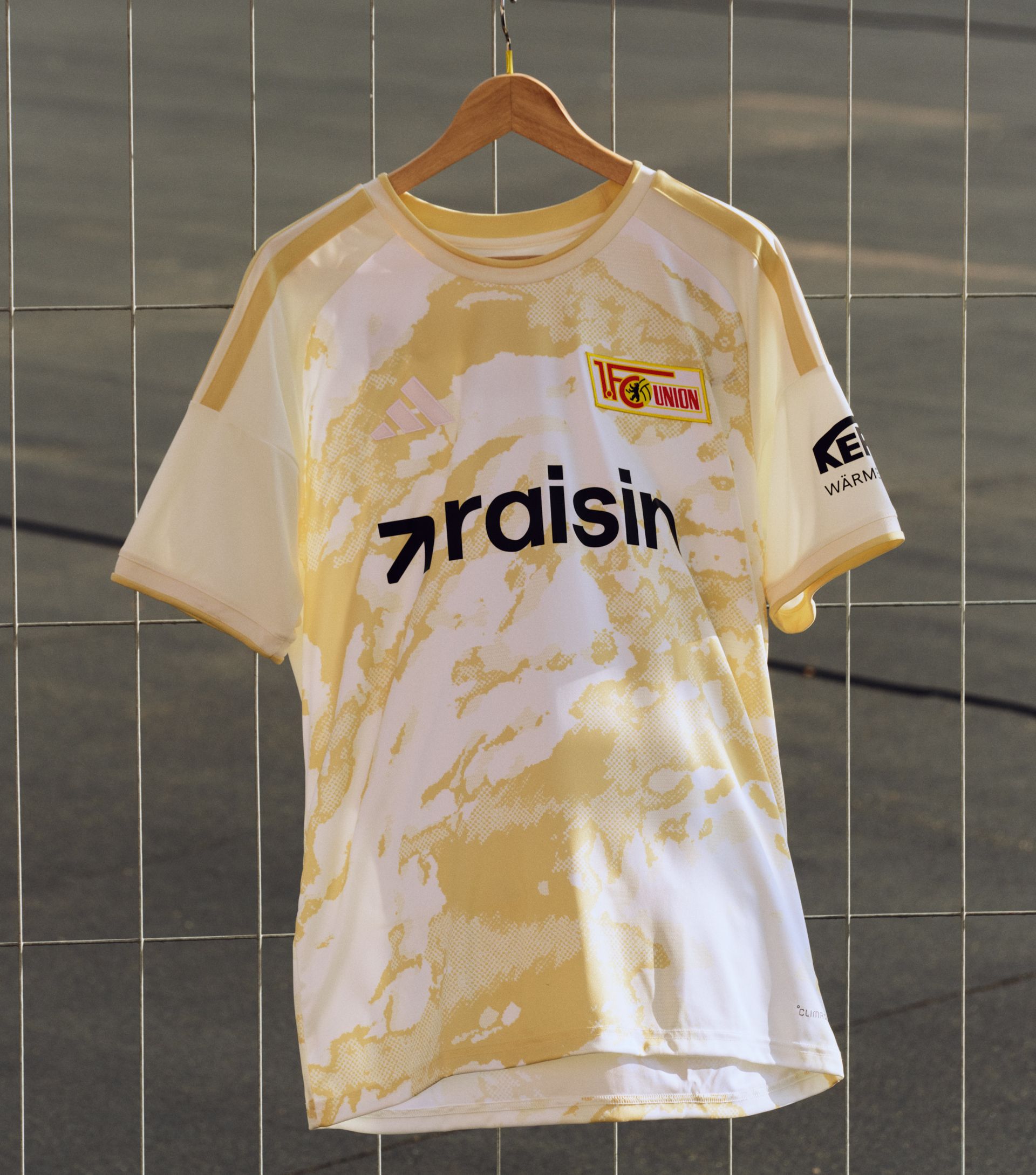 Ein gelbes Fußballtrikot mit dem Aufdruck "UFC Union" und "raisin" in schwarzer Schrift. Hängt an einem Holzkleiderbügel.