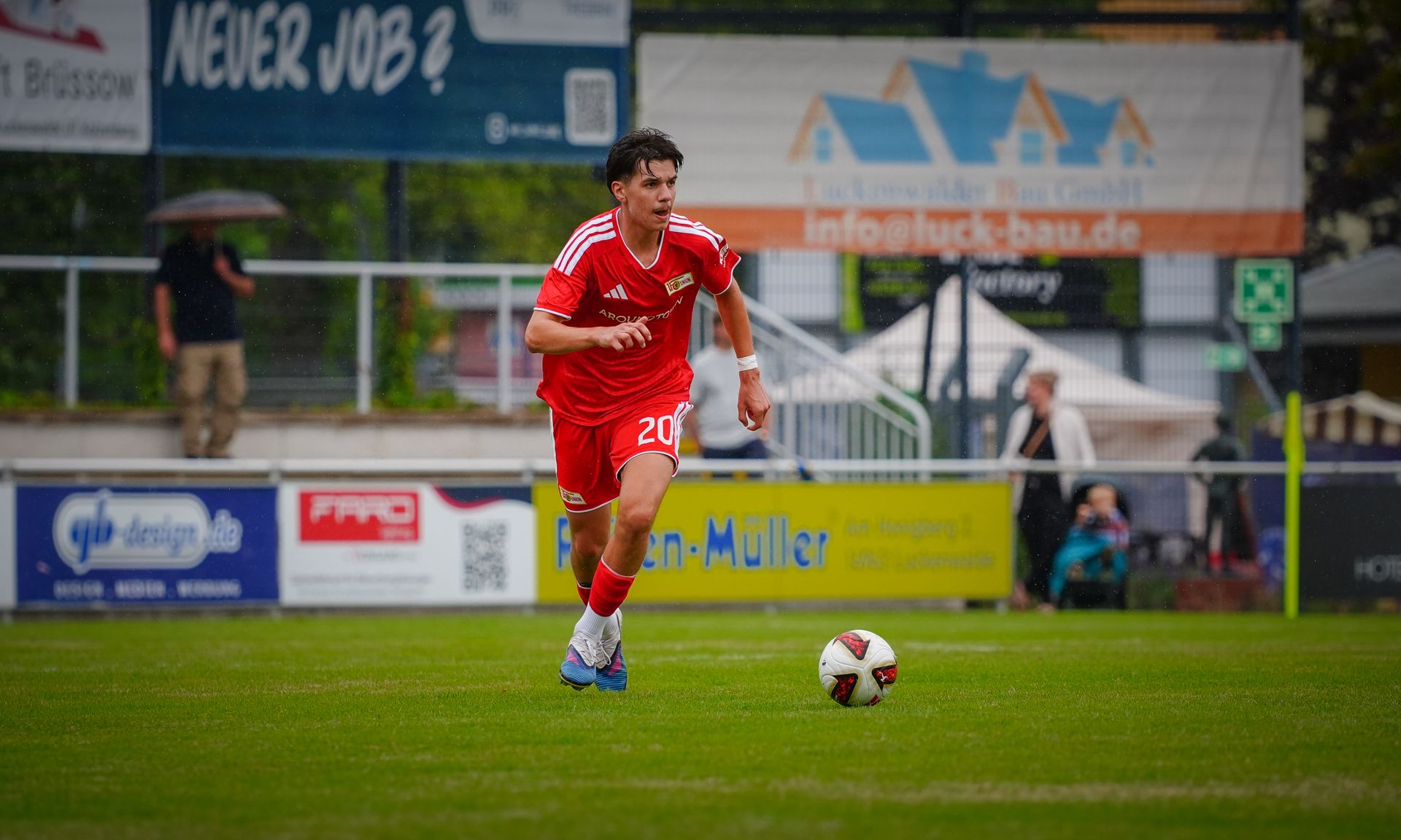 Ein junger Fußballspieler in rotem Trikot sprintet über das Spielfeld auf einen Ball zu.
