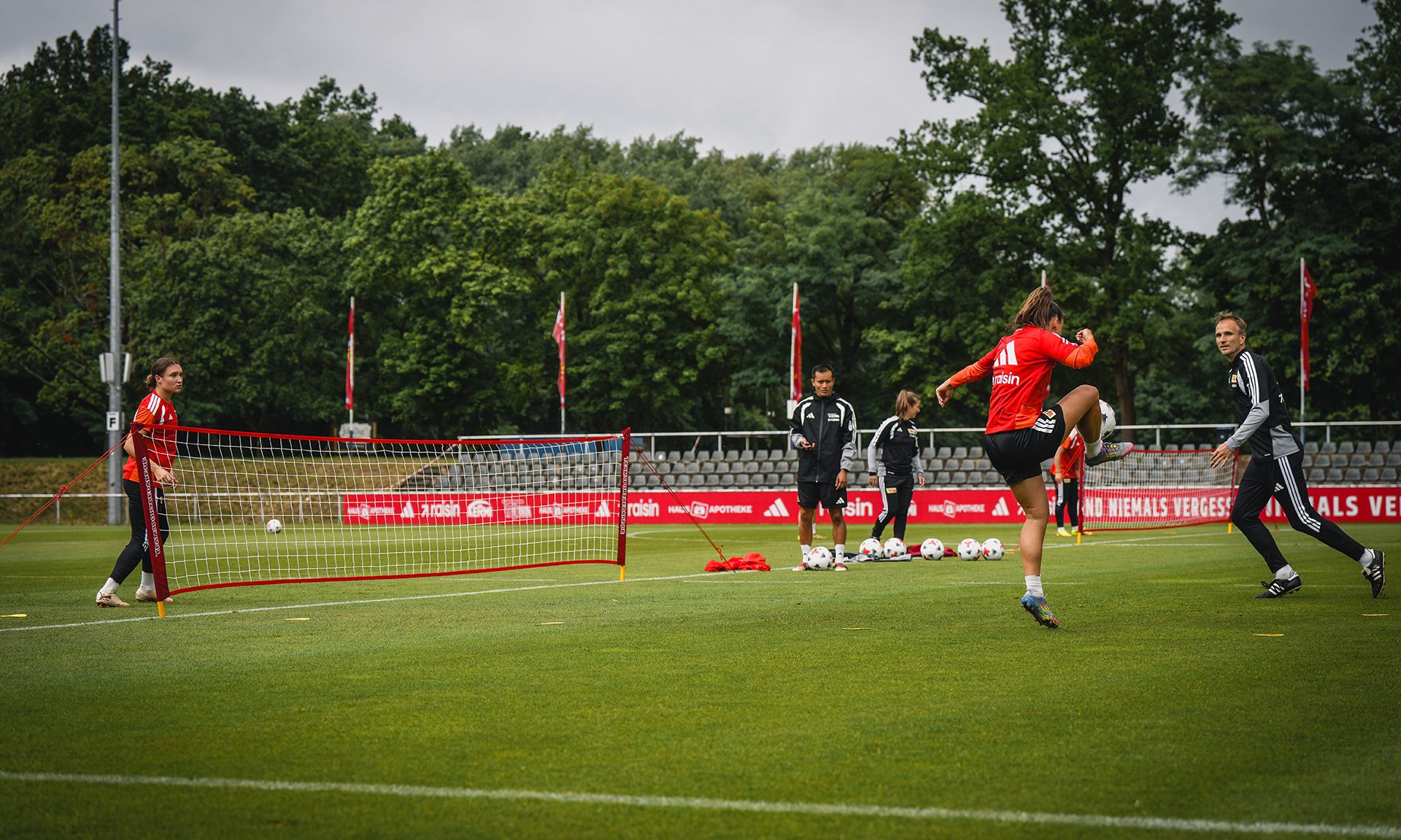 Eine Fußballmannschaft trainiert auf einem Rasenplatz, mit Toren und Trainingsmaterialien im Hintergrund.