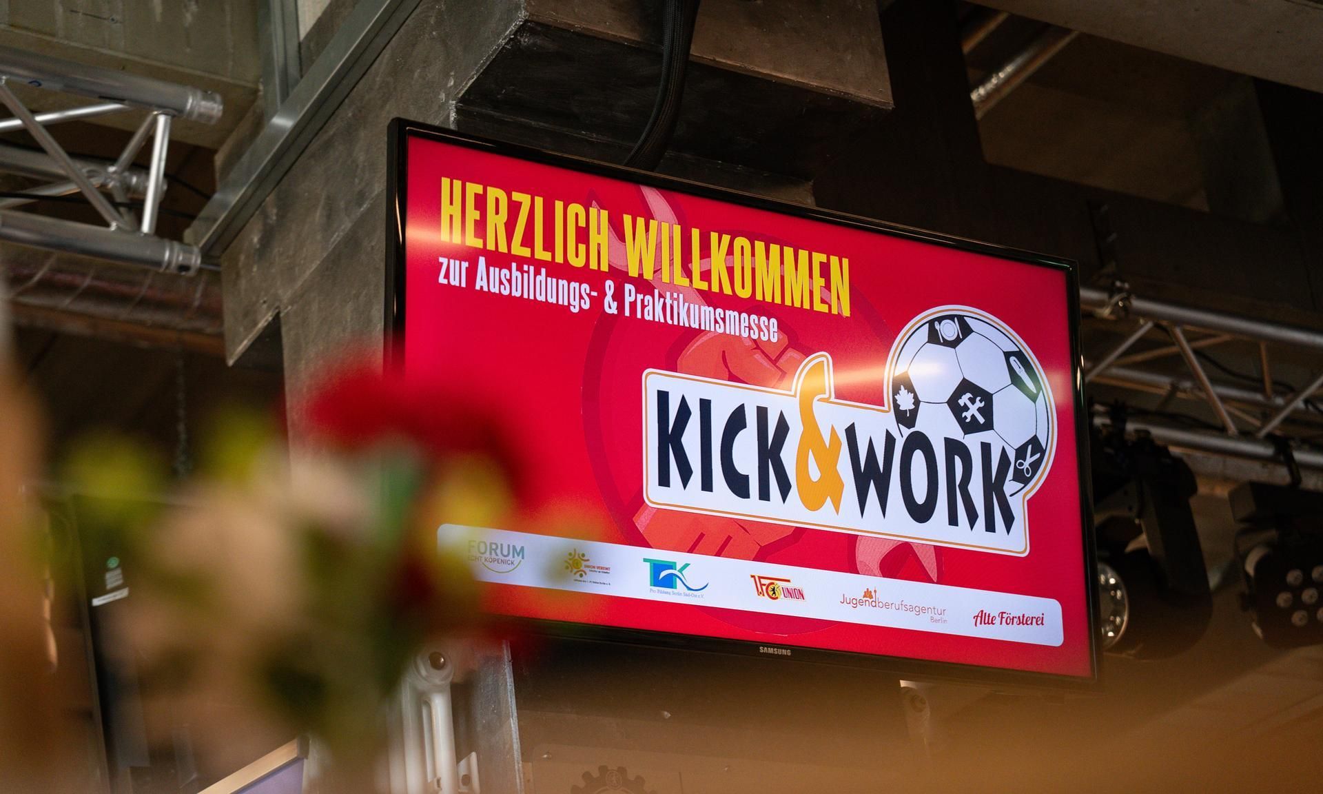 Ein Bildschirm zeigt den Schriftzug "Kick & Work" und den Willkommensgruß zur Ausbildungs- und Praktikumsmesse.