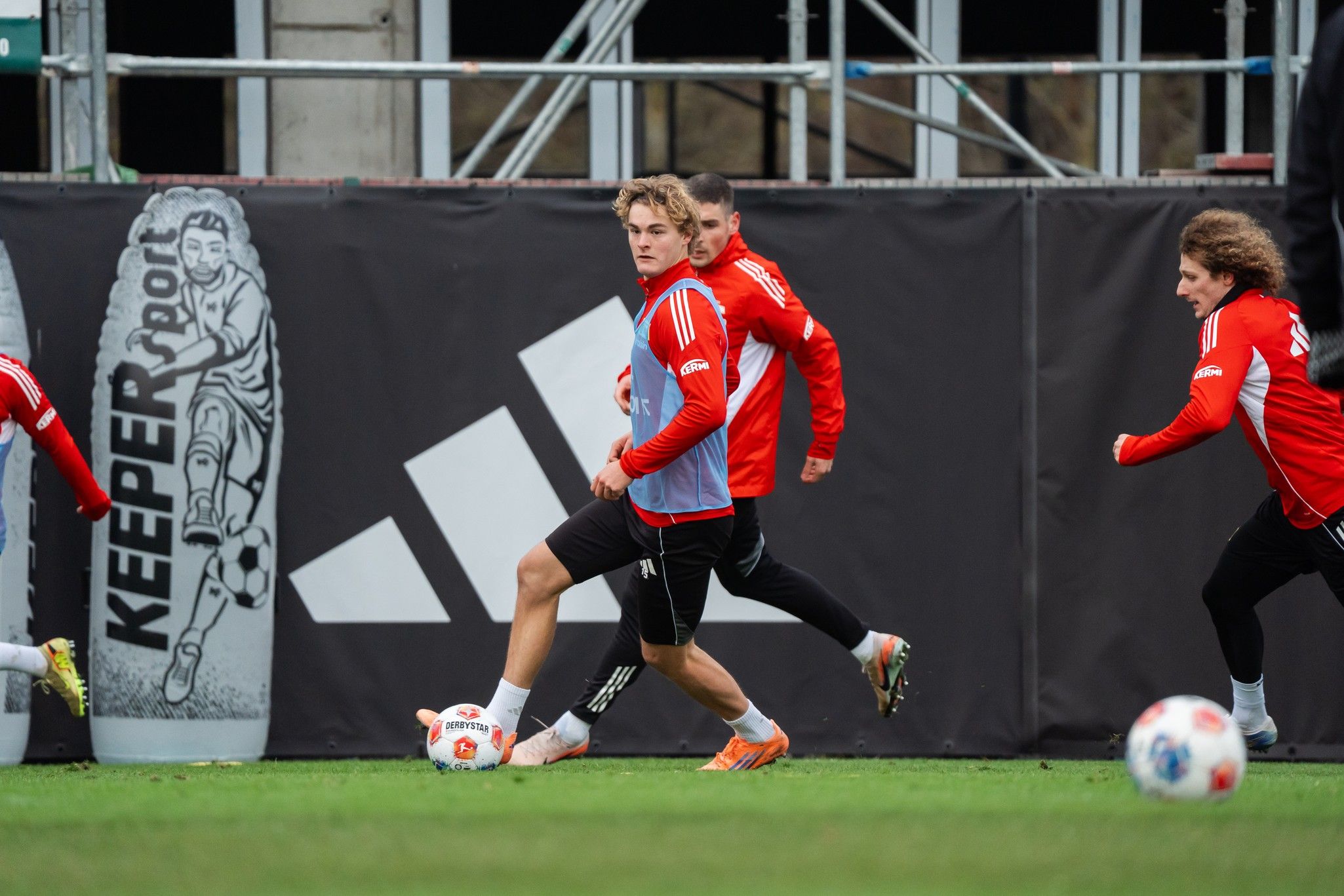Spieler in roten Trikots trainieren auf einem Fußballplatz, während sie den Ball dribbeln und sich bewegen.