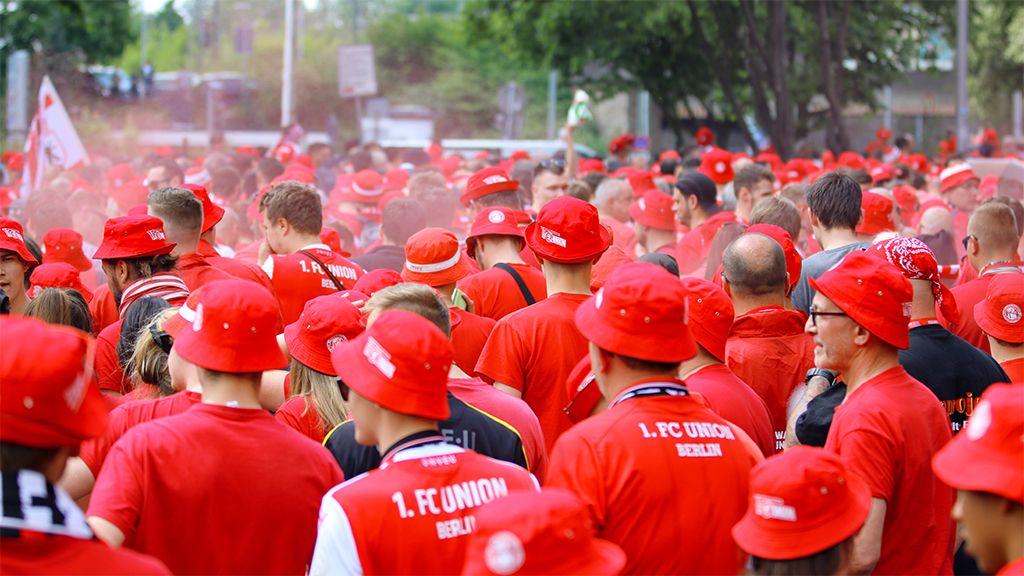 Menschenmenge in roten T-Shirts und roten Hüten, die gemeinsam an einer Veranstaltung teilnehmen, umgeben von Rauch und festlicher Stimmung.