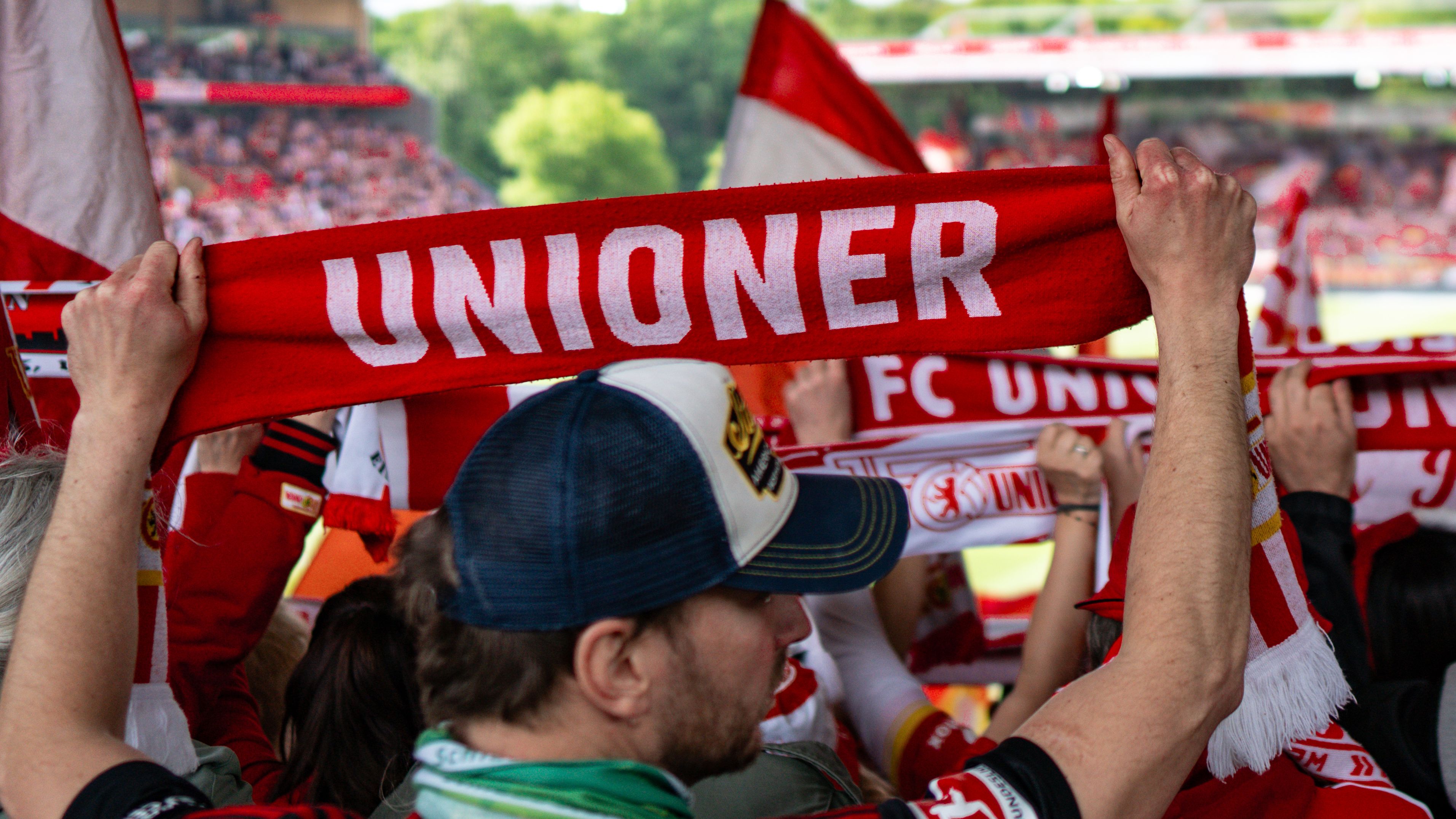 Fan hält ein rotes Schal mit der Aufschrift "UNIONER" in einer jubelnden Menschenmenge.