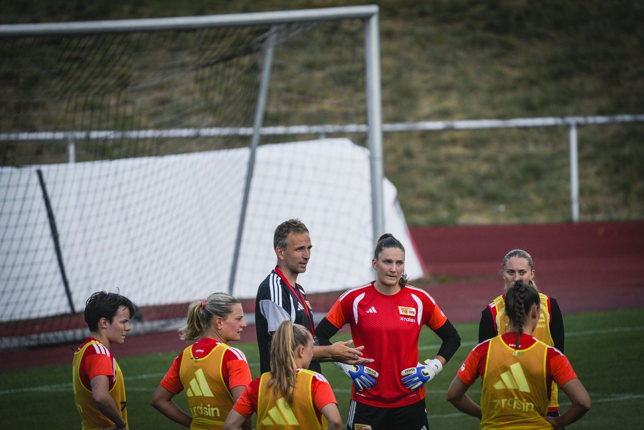 Trainer gibt Anweisungen an eine Gruppe von weiblichen Fußballspielern während des Trainings auf einem Sportplatz.