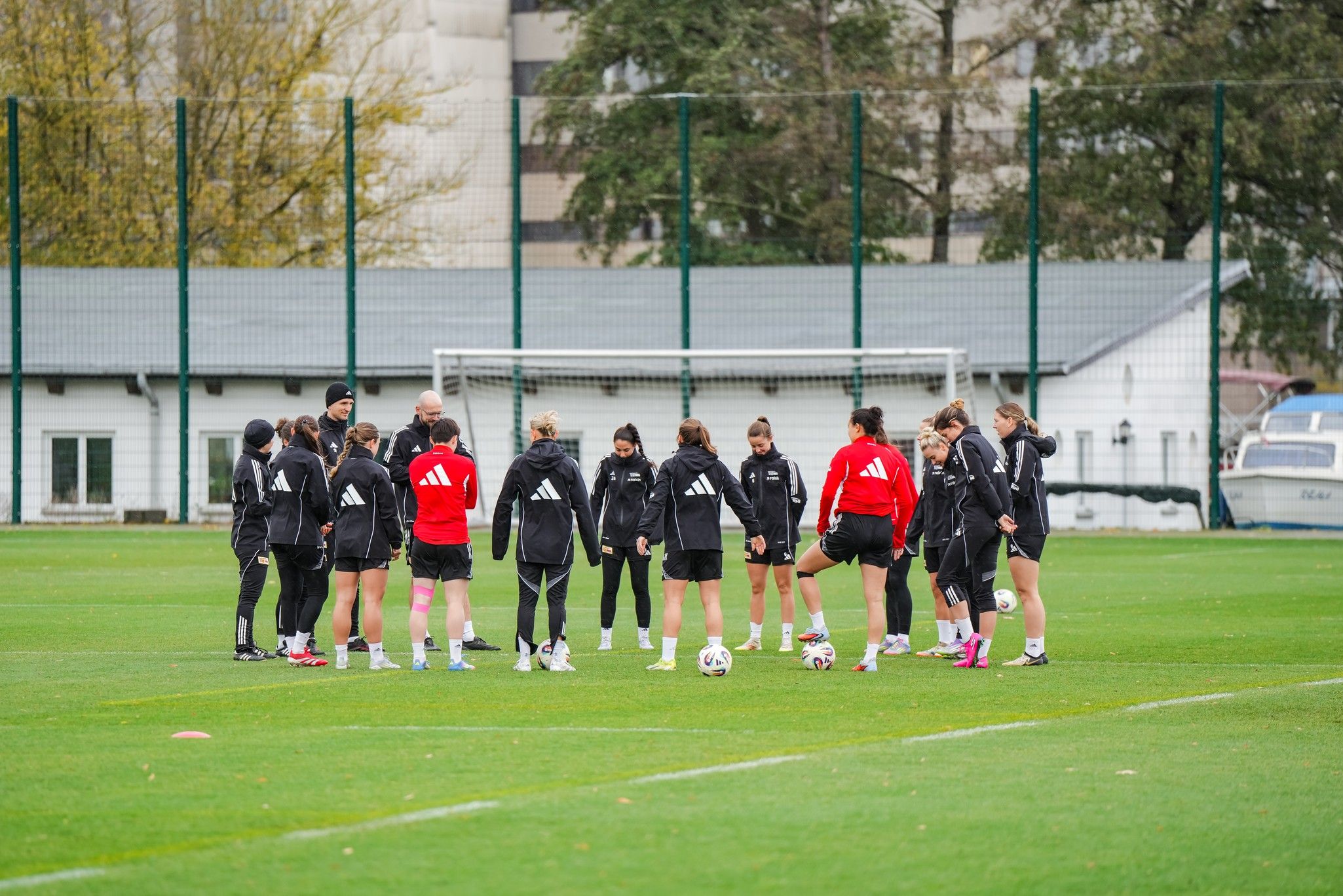 Fußballmannschaft in Trainingskleidung versammelt sich auf einem Rasenplatz, um eine Übung zu besprechen.