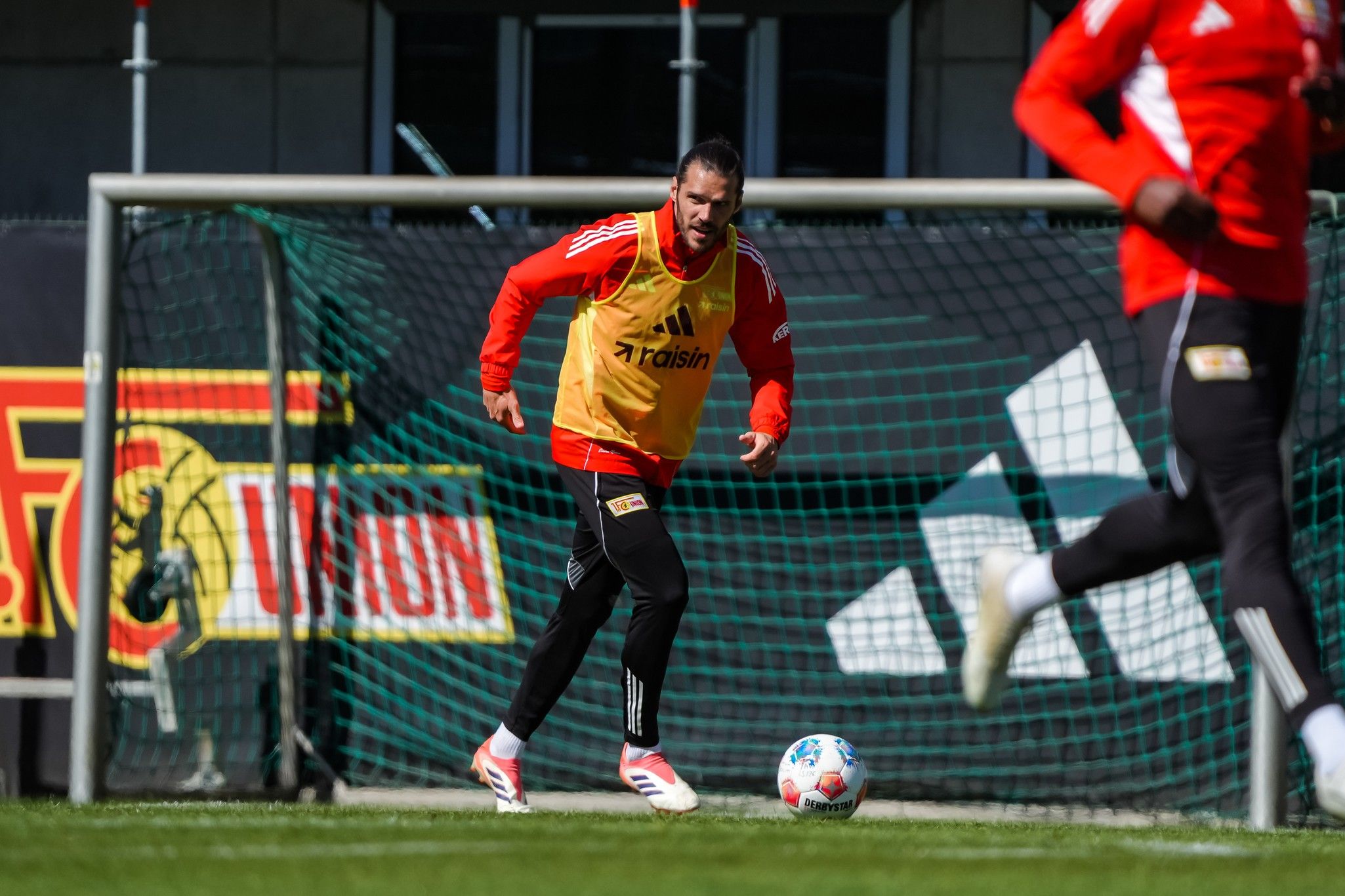 Spieler in Trainingsweste läuft auf einem Fußballfeld während des Trainings, im Hintergrund Werbung und Tor.