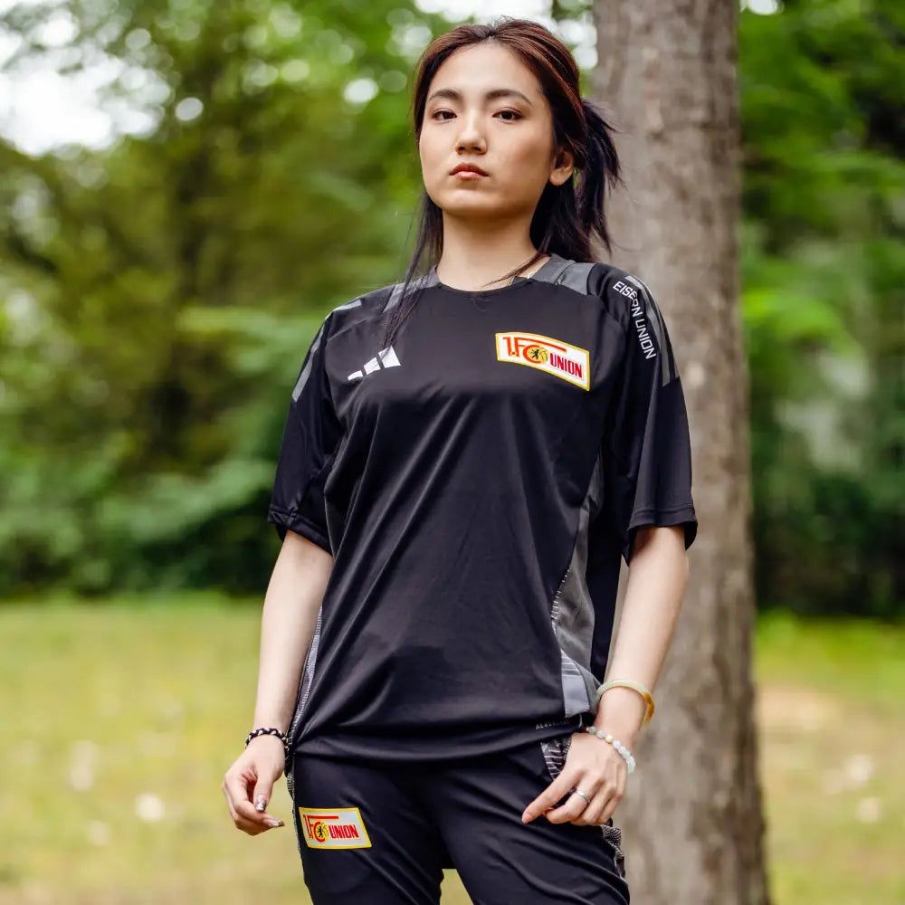 Frau in einem schwarzen Sportoutfit mit dem Logo von 1. FC Union Berlin, steht in einem Park.