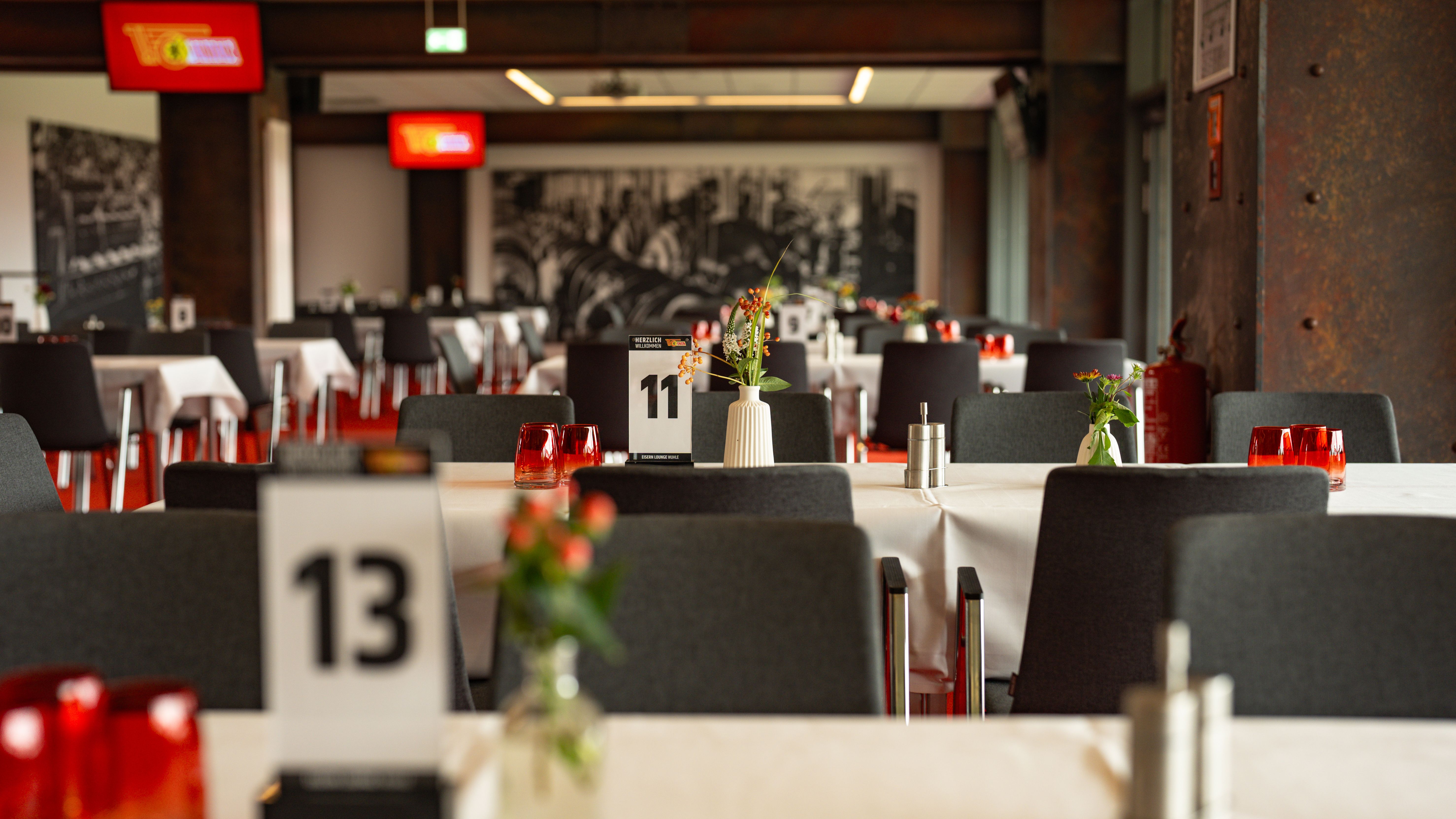 Innenansicht eines Restaurants mit gedeckten Tischen, nummerierten Tischkarten und dekorativen Blumenarrangements.
