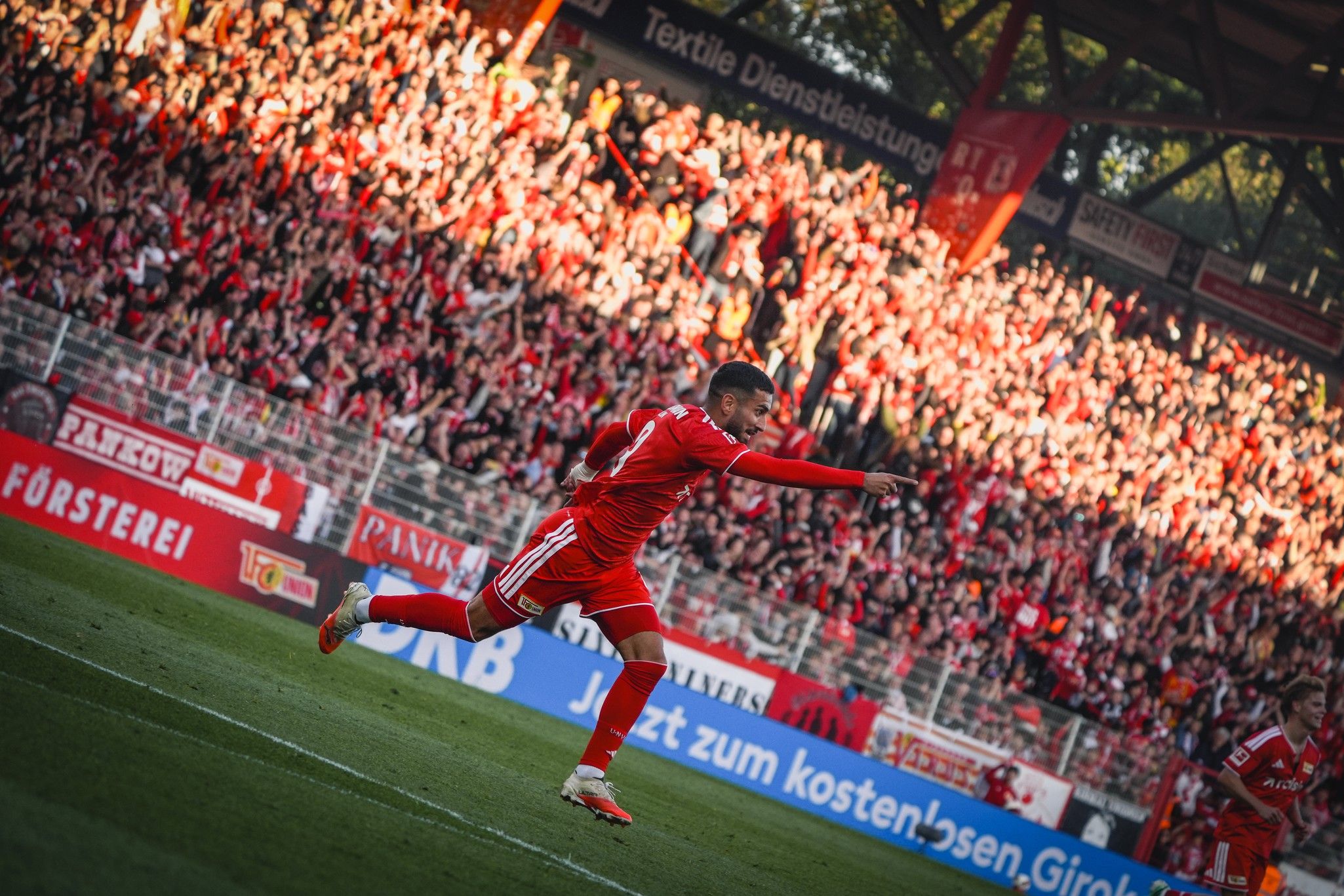 Ein Fußballspieler in rotem Trikot jubelt vor einer jubelnden Menge im Stadion.