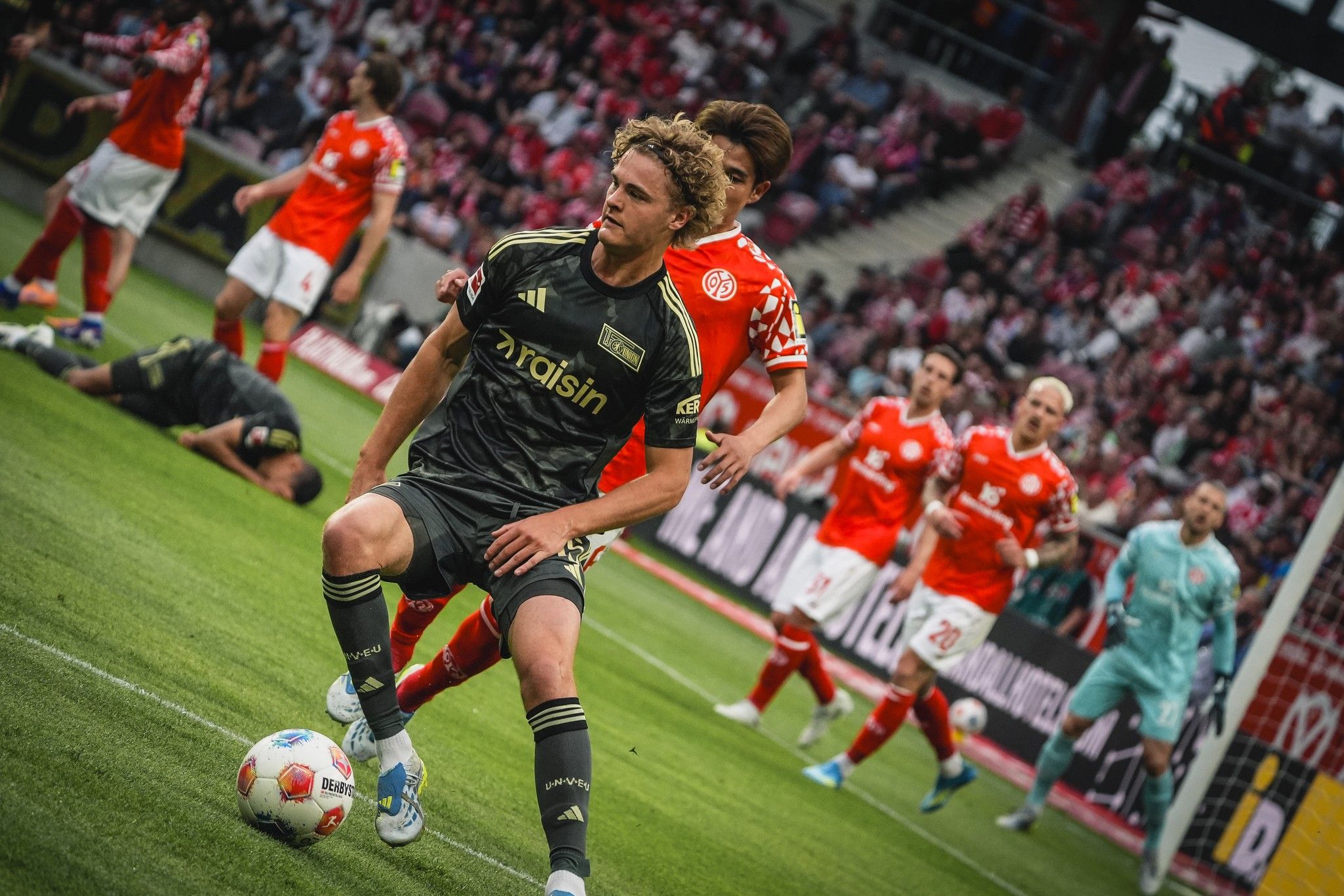 Spielszene im Fußball mit einem Spieler in schwarzem Trikot, der den Ball führt, während Gegner und Teamkollegen im Hintergrund agieren.