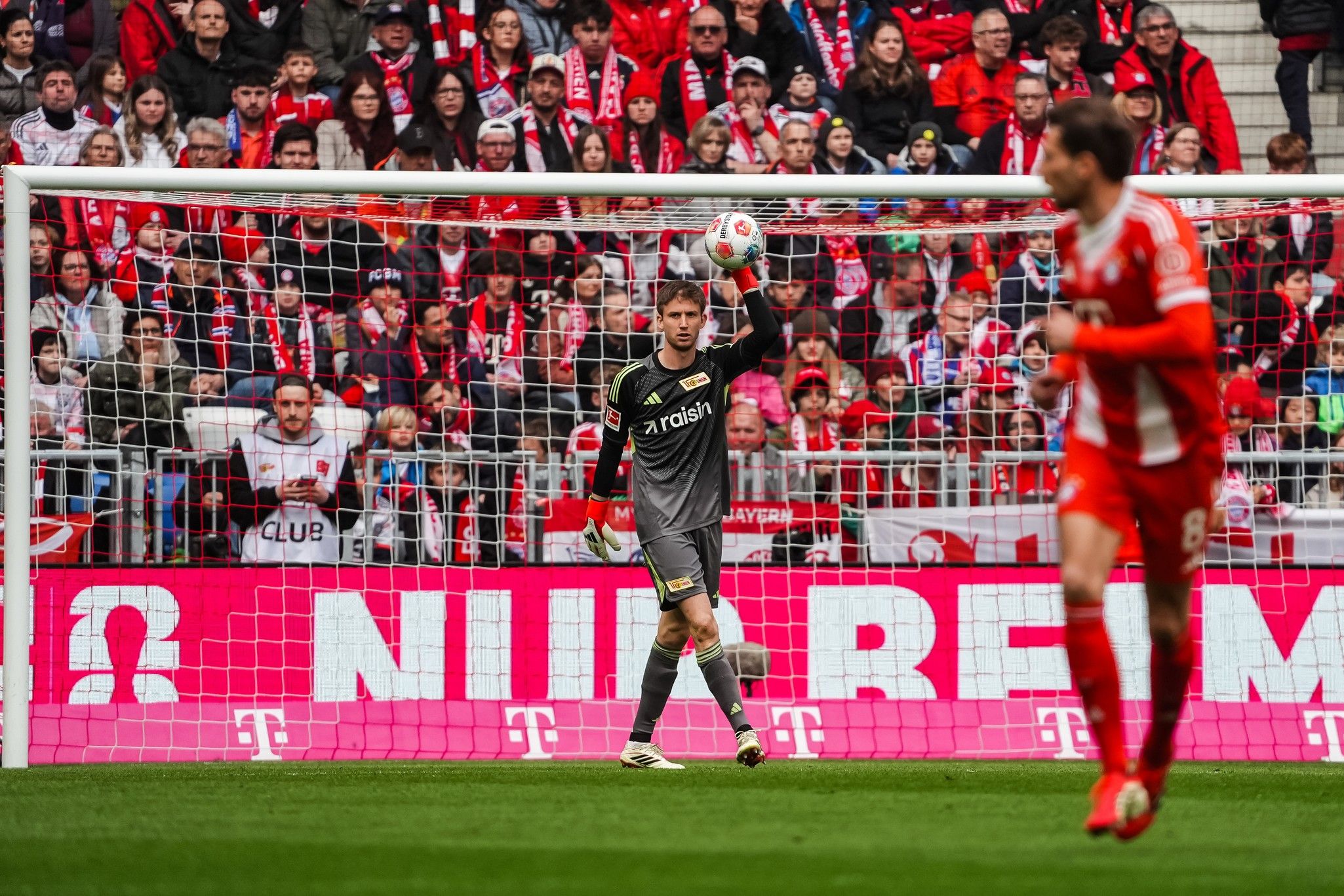 Torhüter in der Aktion, Ball festhaltend, vor jubelndem Publikum in einem Stadion.