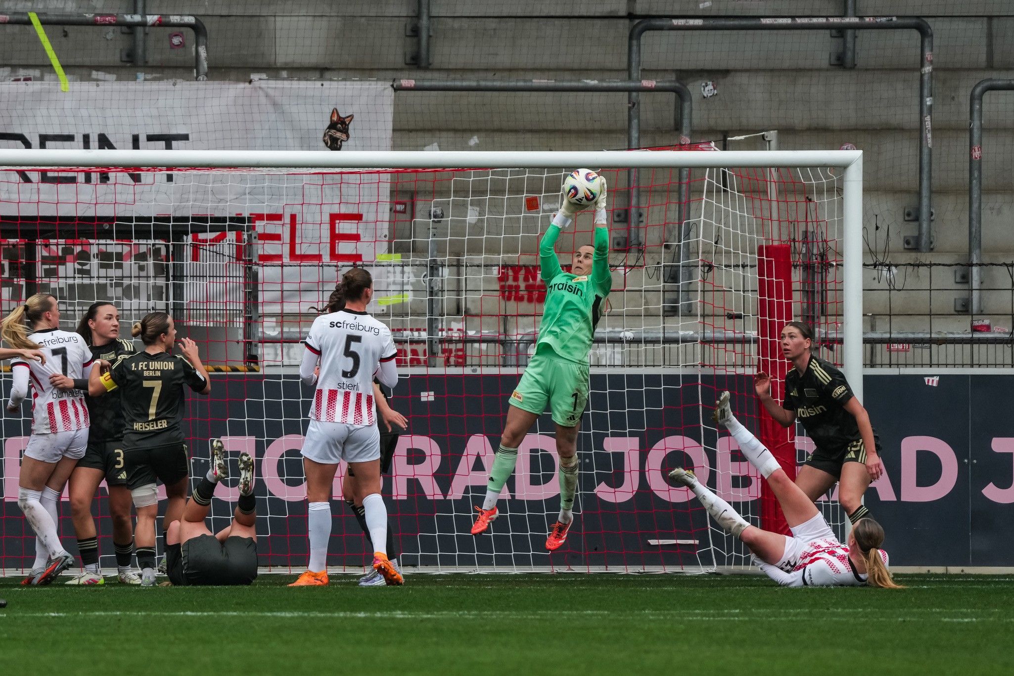 Torwart springt hoch, um einen Ball im Strafraum zu fangen, während Spielerinnen in beiden Trikots um ihn kämpfen.