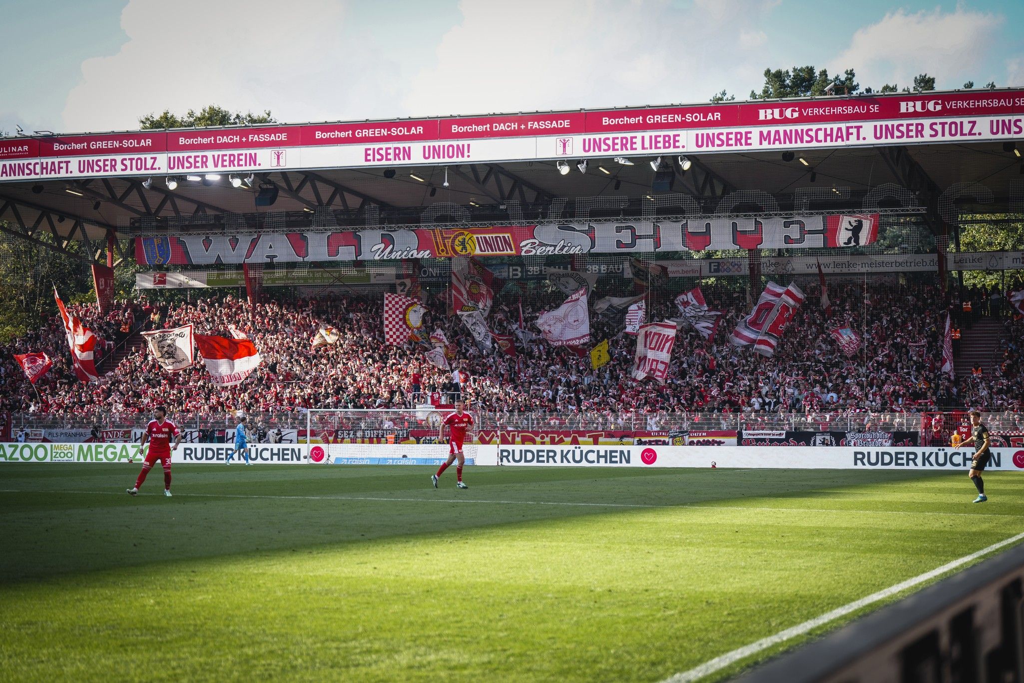 Fußballspiel im Stadion mit jubelnden Fans, Fahnen und einen Spieler auf dem Platz.