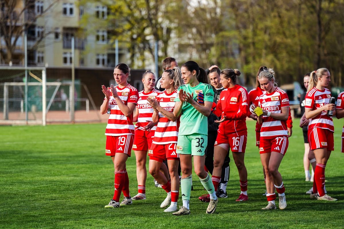 Frauenfußballmannschaft in rot-weißen Trikots applaudiert auf dem Platz nach einem Spiel.