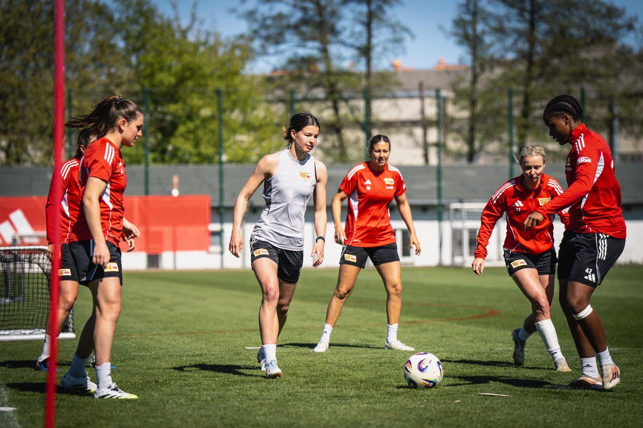 Fünf Fußballspielerinnen in Training, dribbeln und passen den Ball auf einem grünen Rasenplatz.