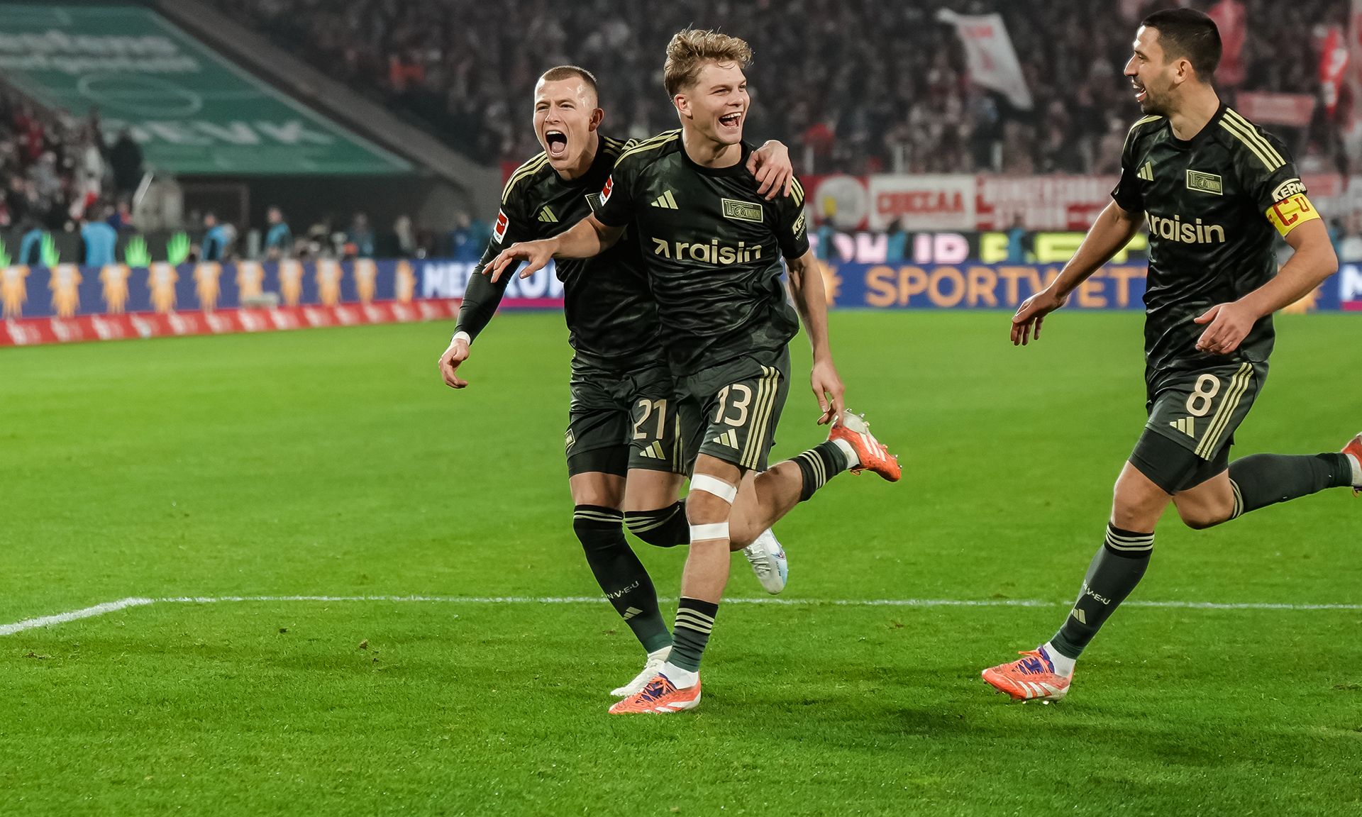 Fußballspieler in schwarzen Trikots feiern einen Torerfolg auf dem Spielfeld.