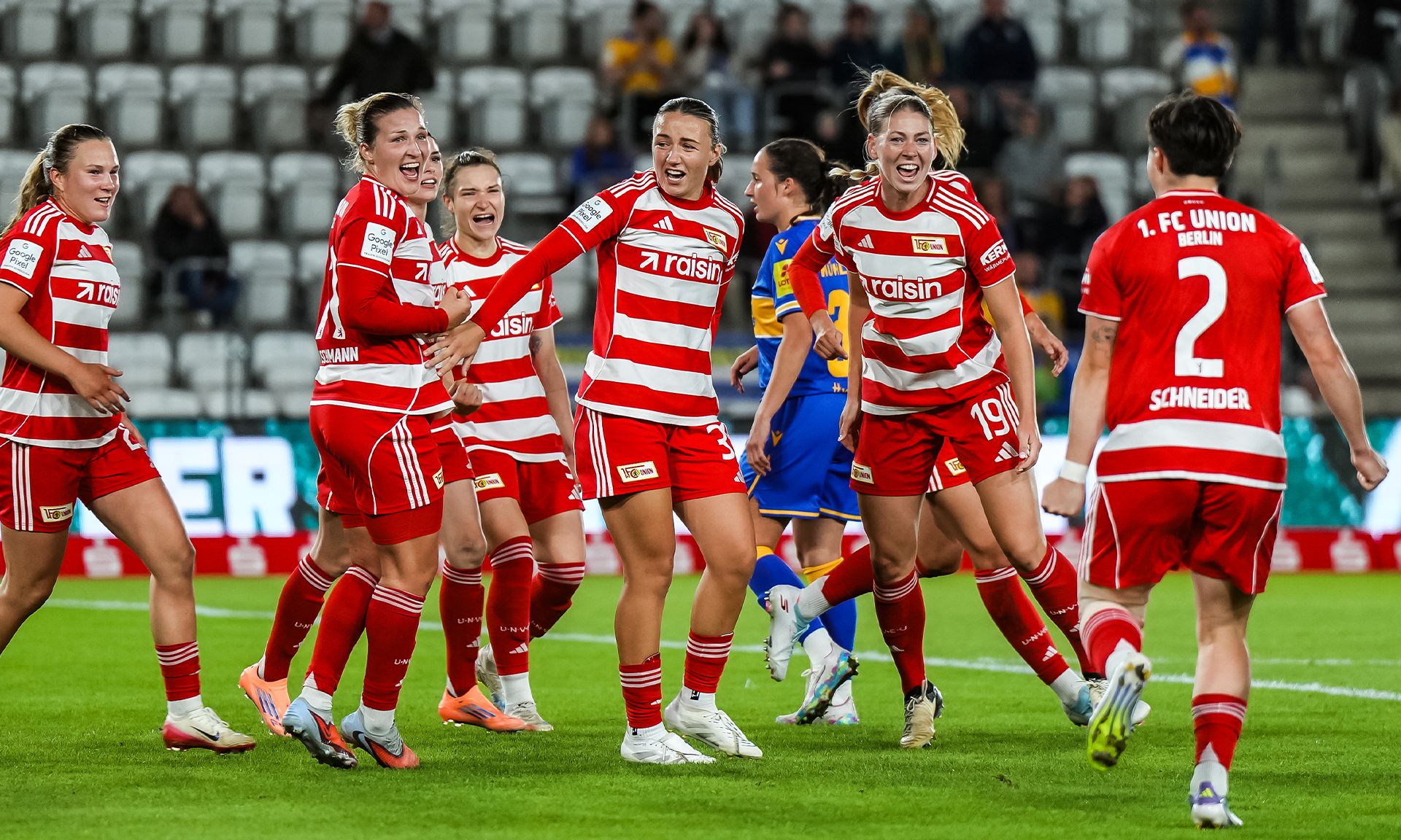 Eine Gruppe von Fußballspielerinnen in roten und weißen Trikots feiert jubelnd auf dem Spielfeld.