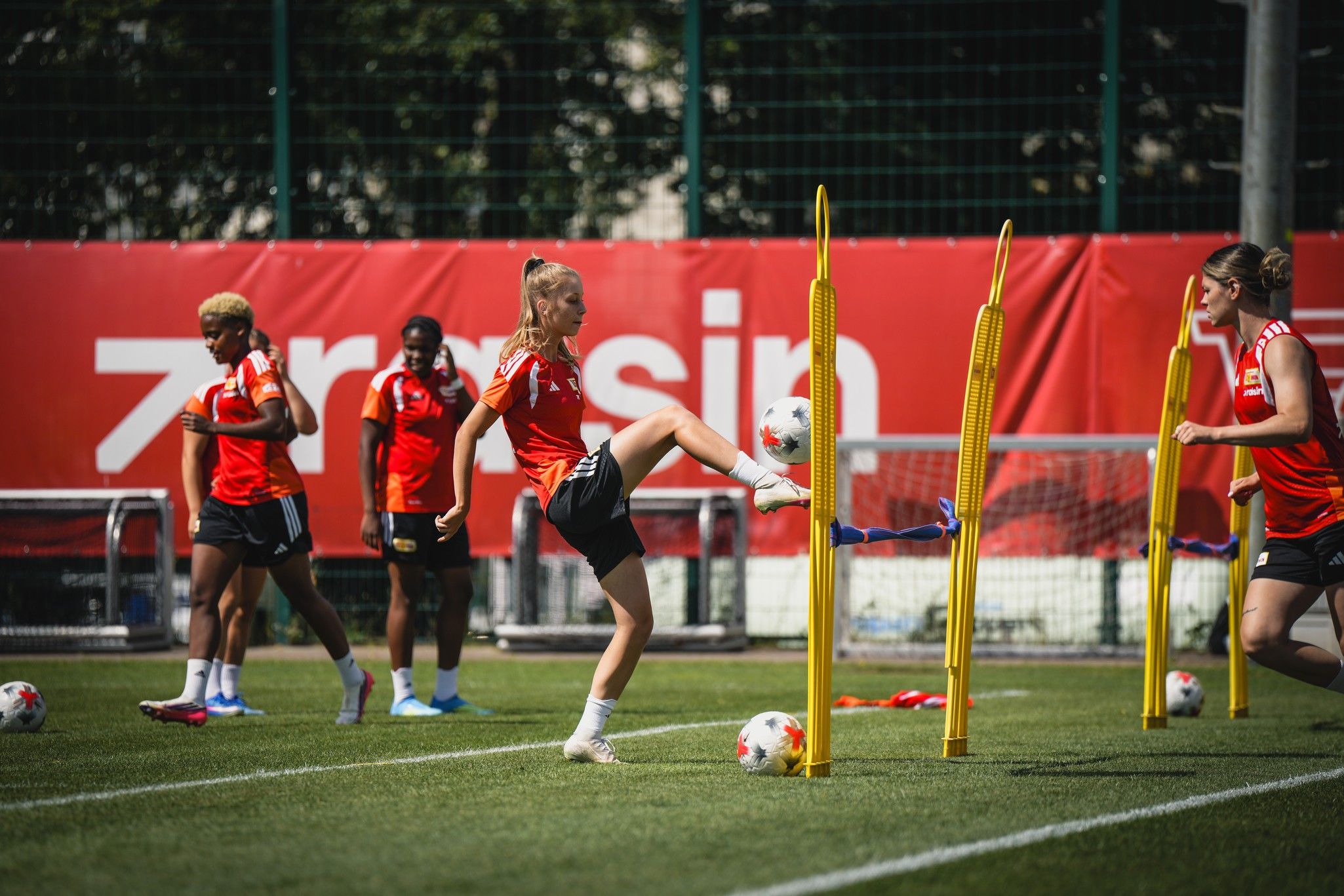 Eine Sportlerin übt beim Training mit Hütchen, während andere Spielerinnen im Hintergrund zuschauen.