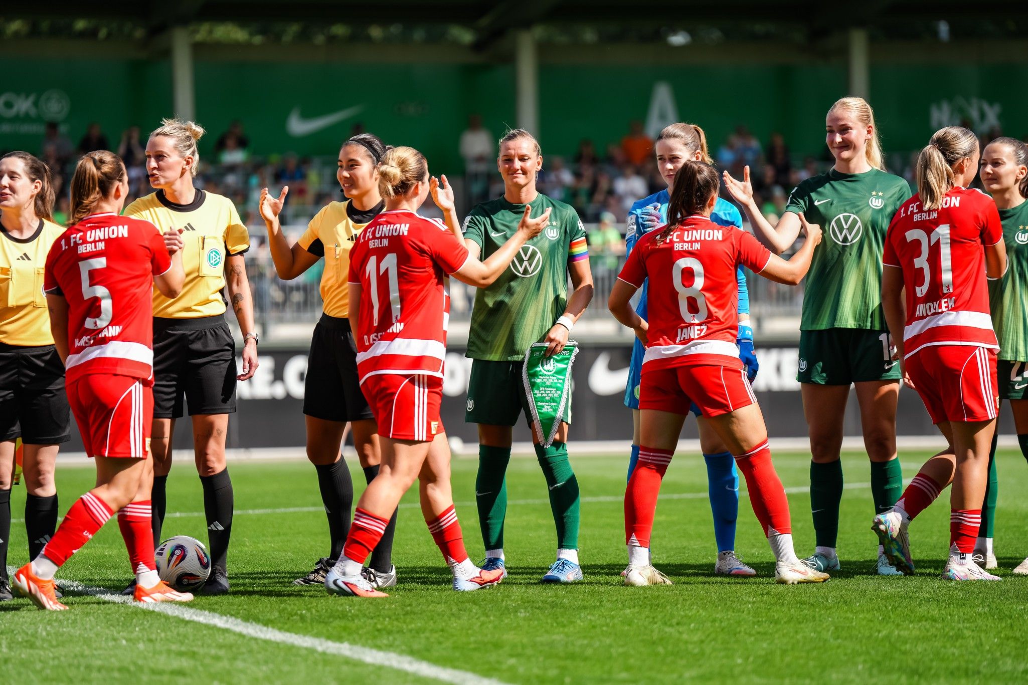 Spielerinnen des FC Union Berlin und Schiedsrichterinnen vor dem Spiel, lächeln und begrüßen sich auf dem Fußballfeld.