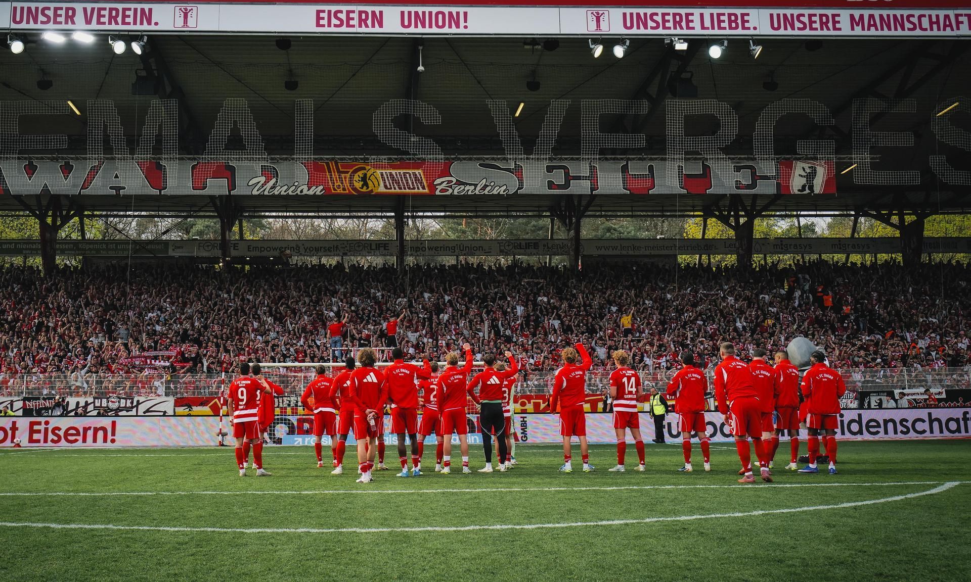 Fußballmannschaft in roten Trikots feiert vor jubelndem Publikum im Stadion.