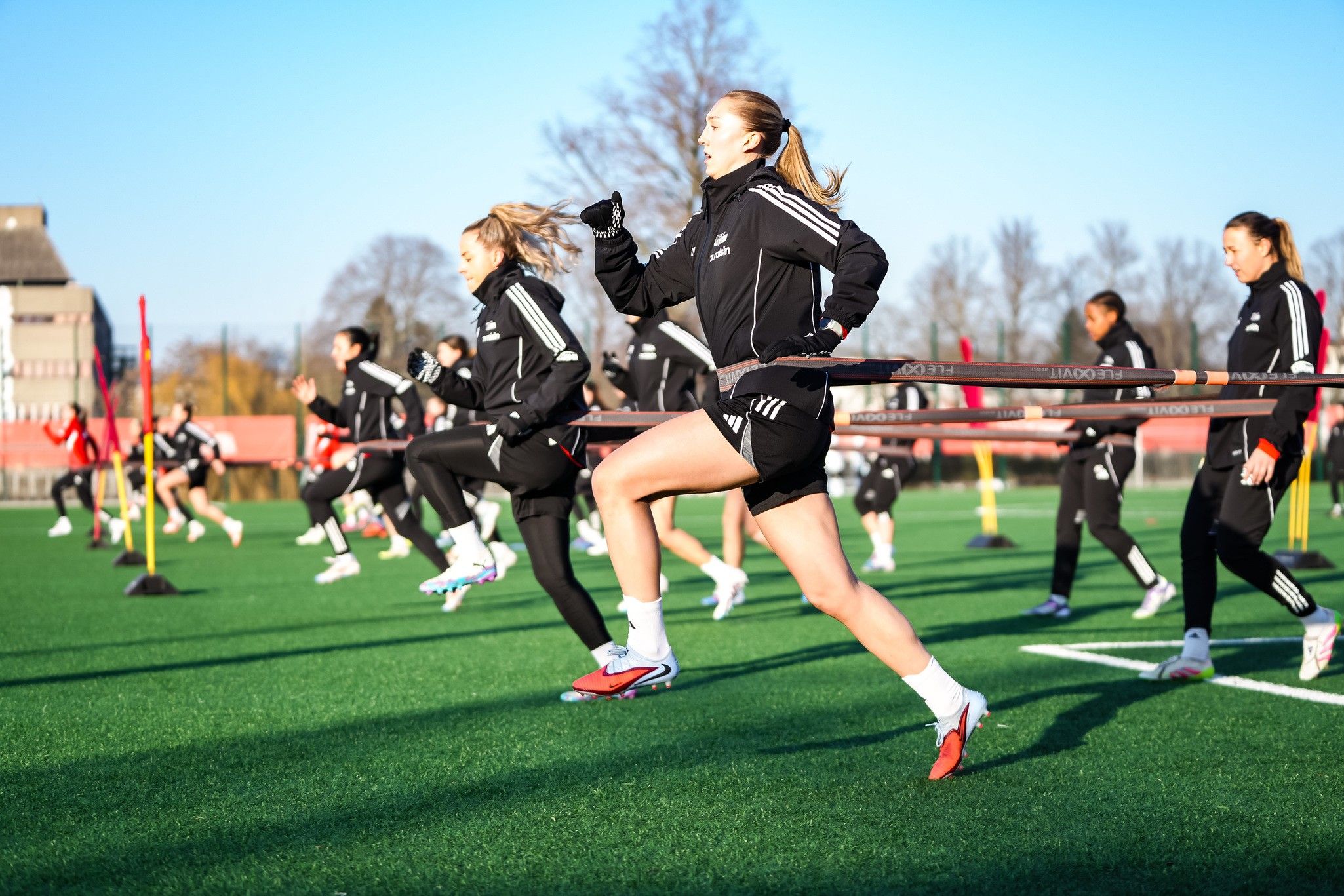 Sportlerinnen trainieren auf einem grünen Platz, während sie einen Widerstandsbänder nutzen, um ihre Schnelligkeit zu verbessern.