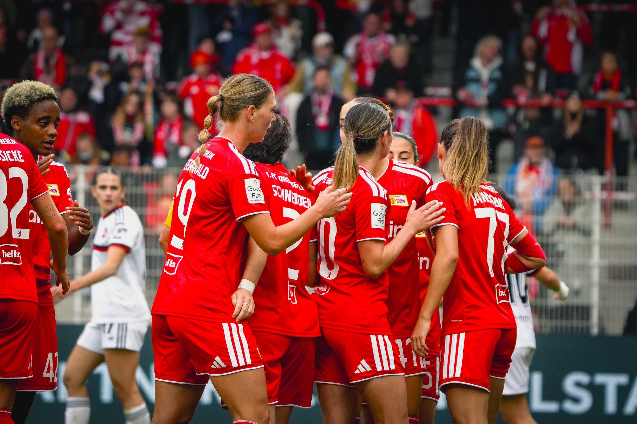 Eine Gruppe von Fußballspielerinnen in roten Trikots feiert einen Torerfolg zusammen in einem Stadion.