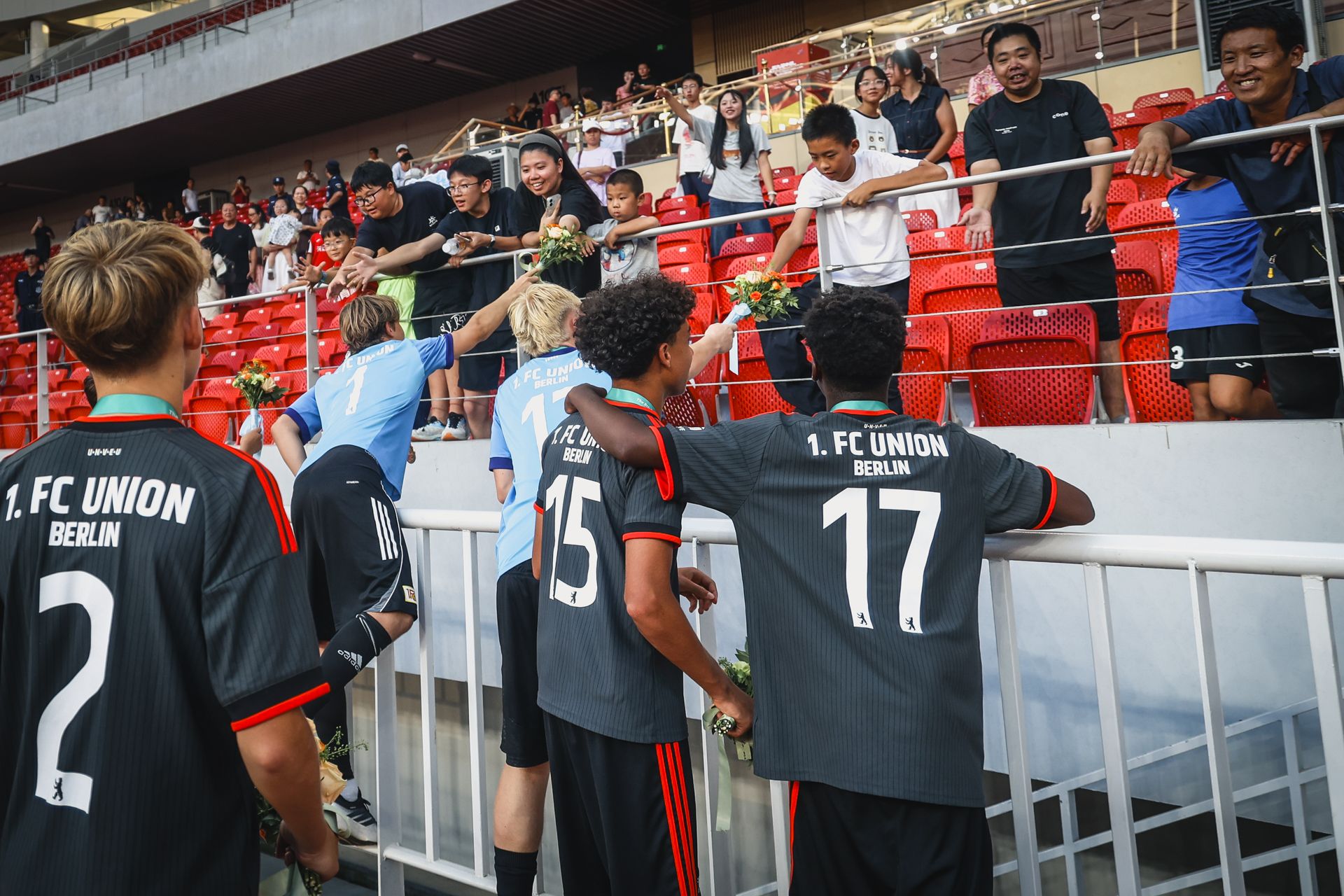 Spieler des 1. FC Union Berlin feiern mit Fans auf der Tribüne, während sie Blumen verschenken.