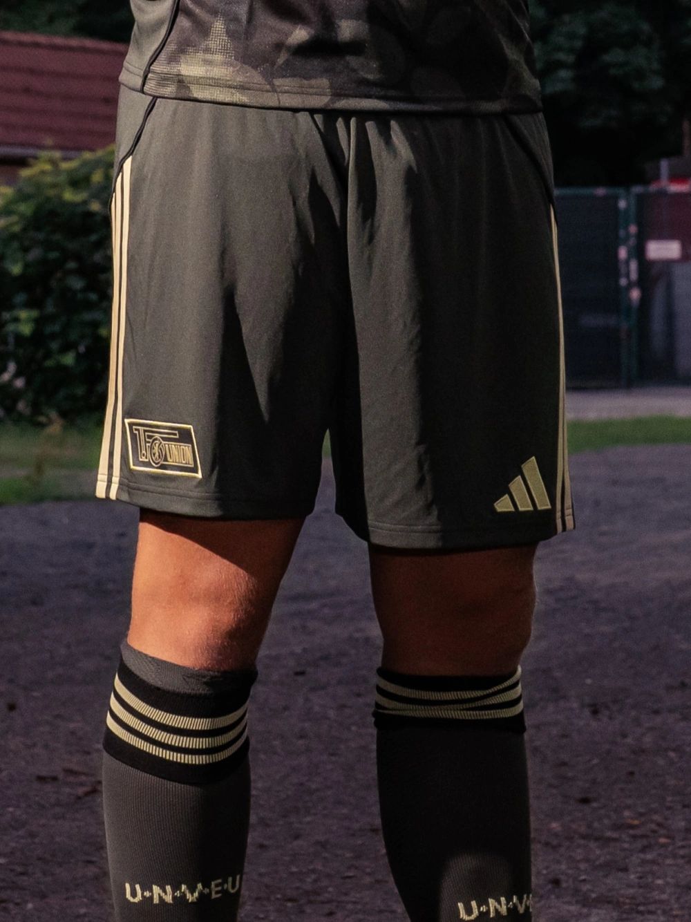 Sportliche Shorts in Dunkelgrau mit goldenen Akzenten und einem Adidas-Logo, getragen von einem Spieler.