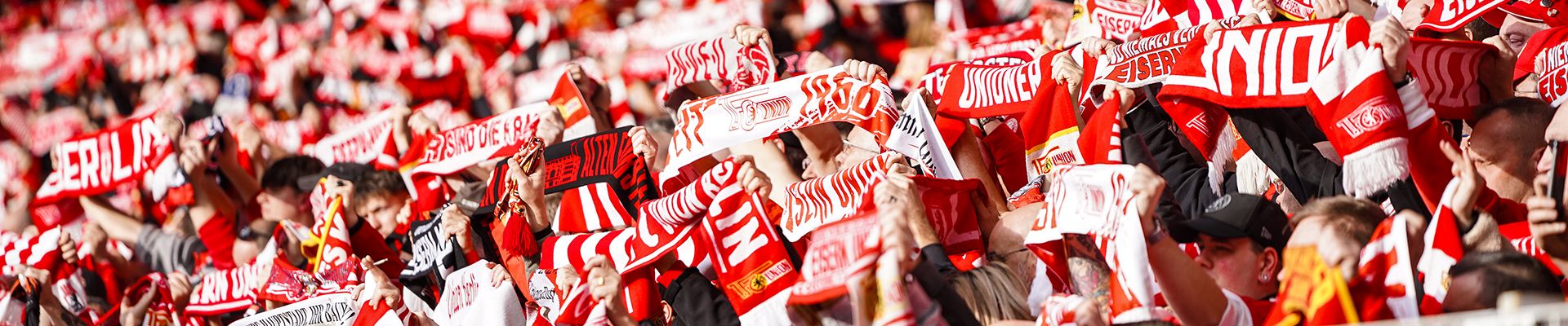 Ein begeistertes Publikum in einem Stadion hält rote und weiße Schals hoch, um ihre Mannschaft zu unterstützen.