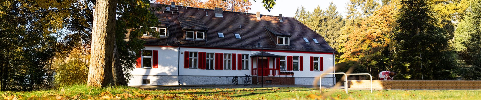Ein traditionelles, mehrstöckiges Haus mit rotem Dach und weißen Wänden, umgeben von Bäumen und grünem Rasen.