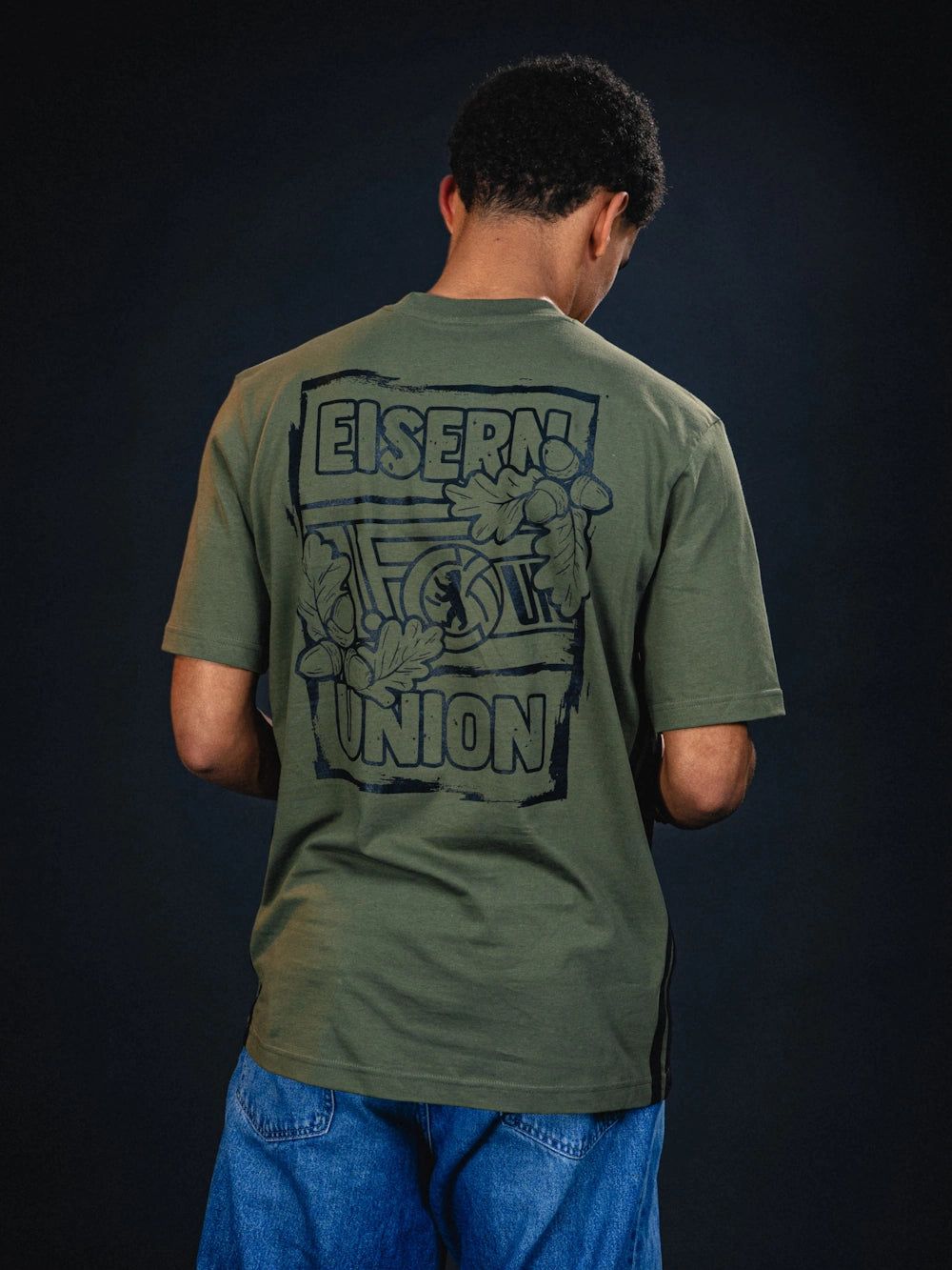 Mann von hinten in olivgrünem T-Shirt mit großem, grafischen Print "EISERN! UNION" auf dem Rücken.