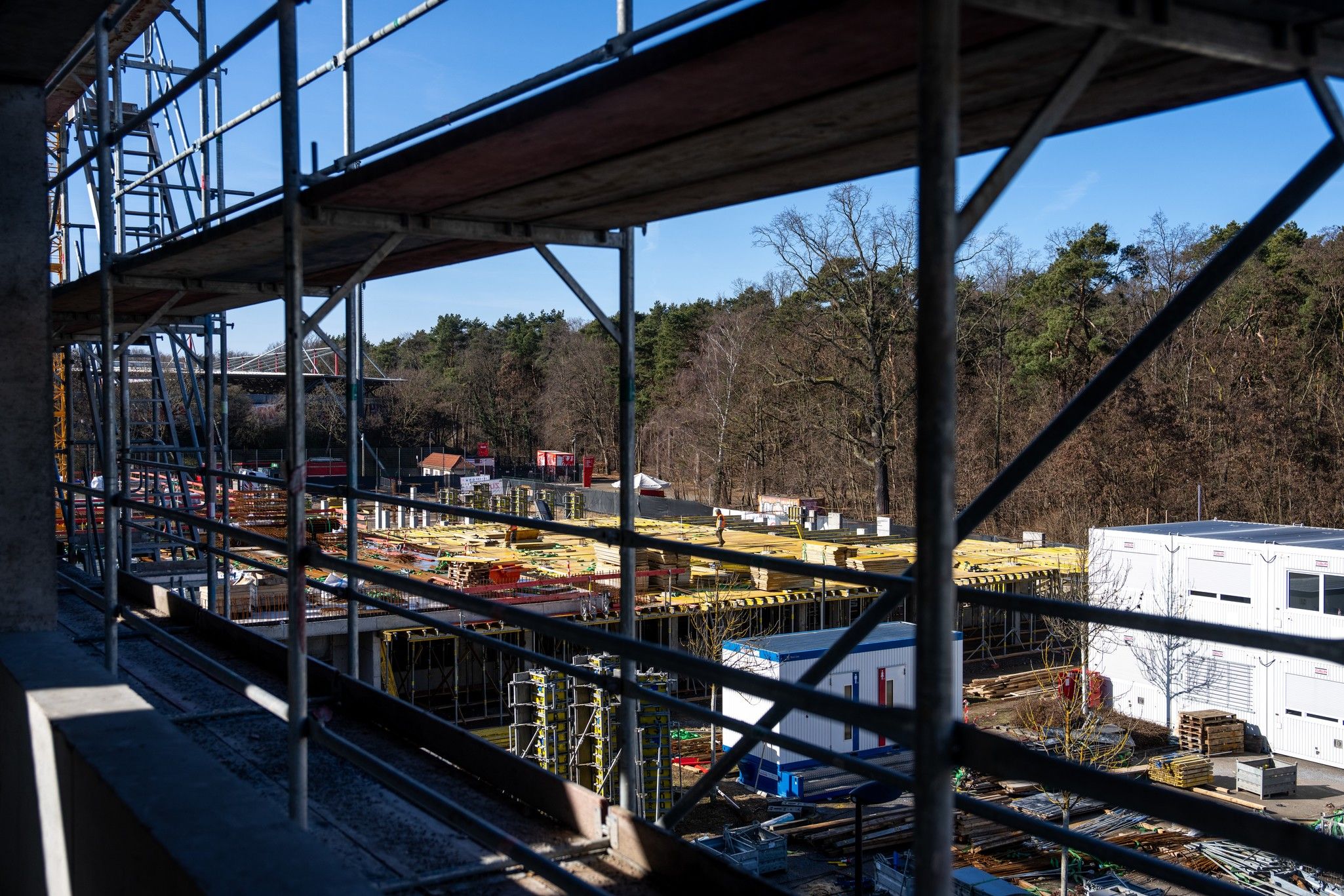 Blick auf eine Baustelle mit Gerüst, Holzgestellen und Bäumen im Hintergrund an einem sonnigen Tag.