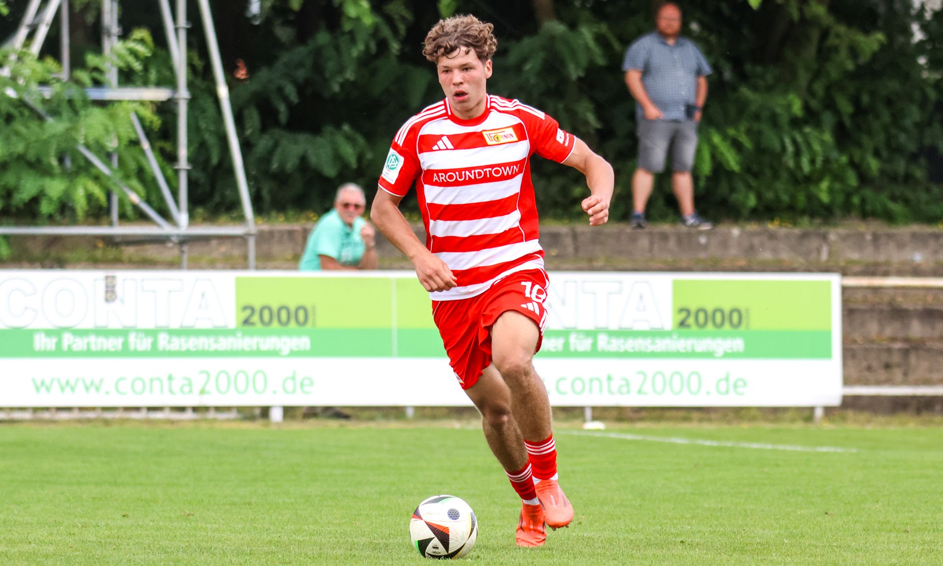 Ein junger Fußballspieler in roter und weißer Stripes-Passion läuft mit dem Ball auf einem Fußballfeld.