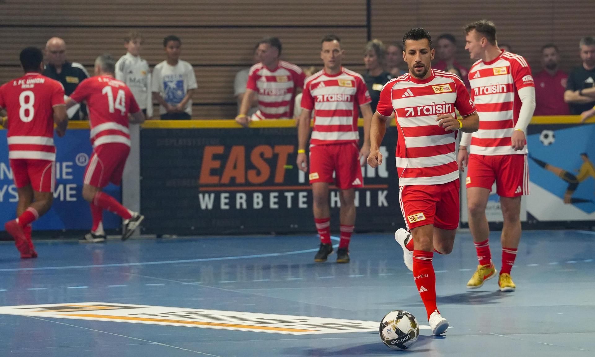Fußballspiel mit Spielern des Teams in roten Streifen-Trikots auf dem Feld, während sie sich auf das Spiel vorbereiten.