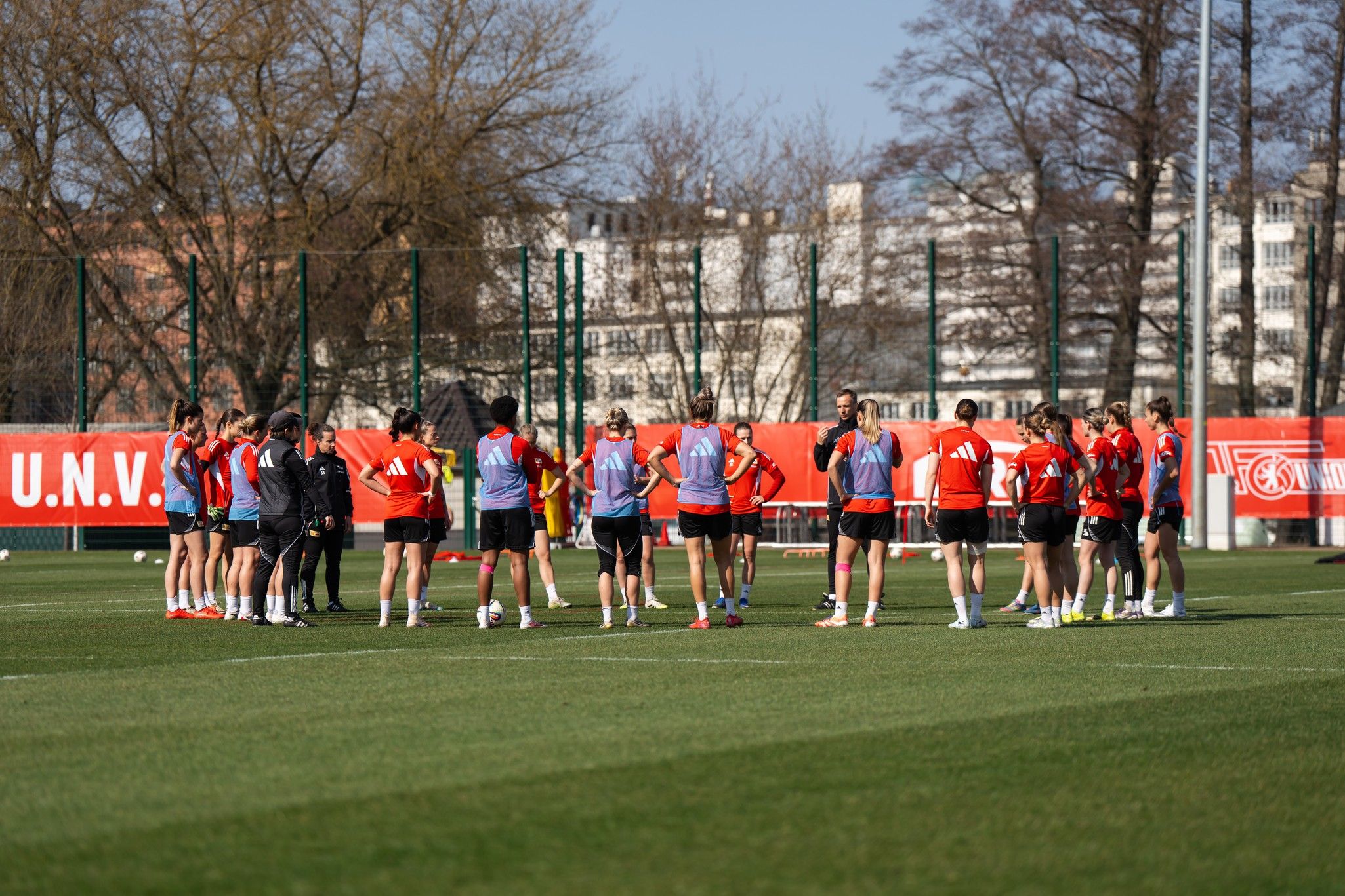 Mannschaftstraining auf einem Fußballplatz, Spieler versammelt sich in einem Kreis, um Anweisungen zu erhalten.