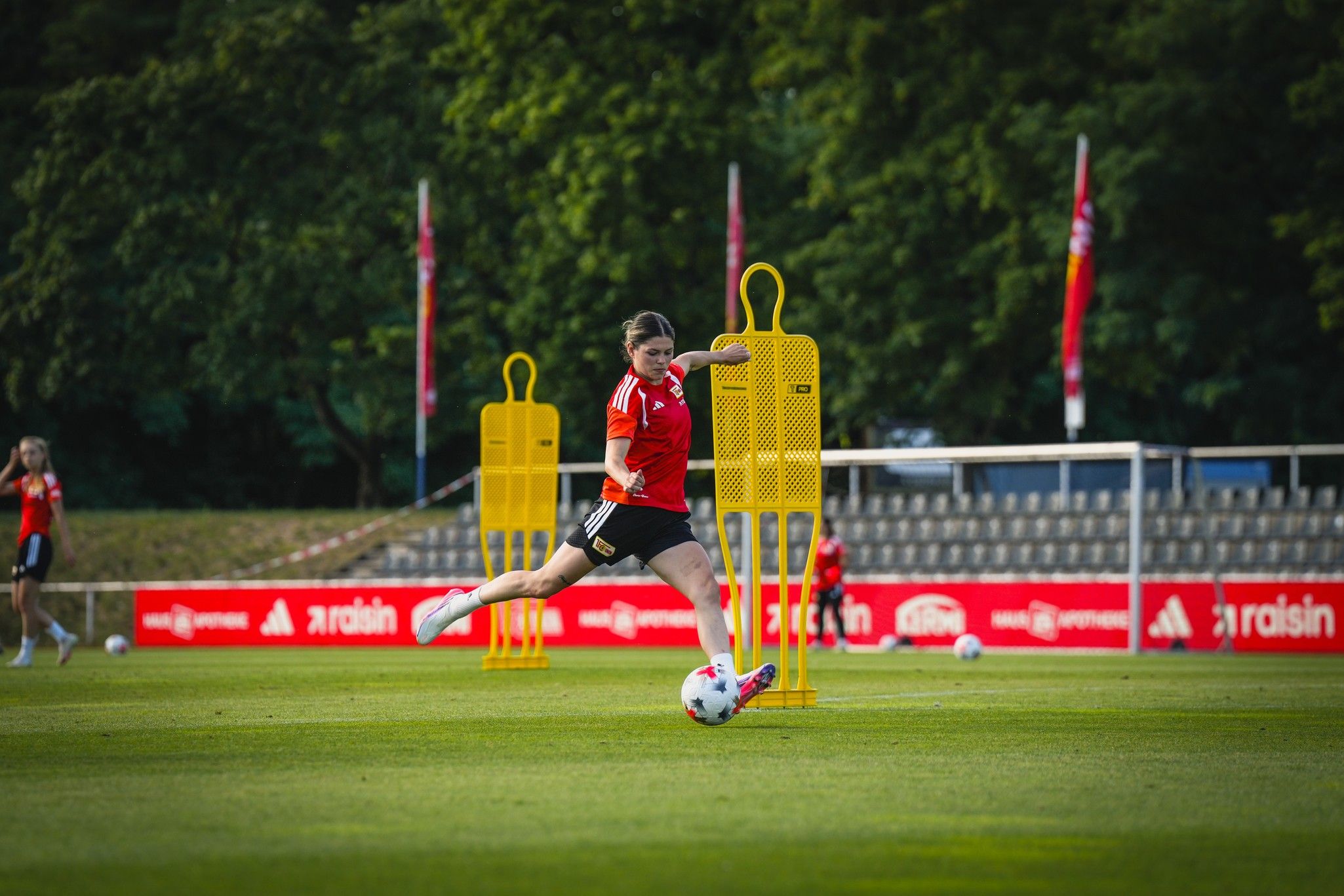 Eine Fußballspielerin in rotem Trikot schießt den Ball an einem Trainingsfeld mit Trainingsdummys vorbei.