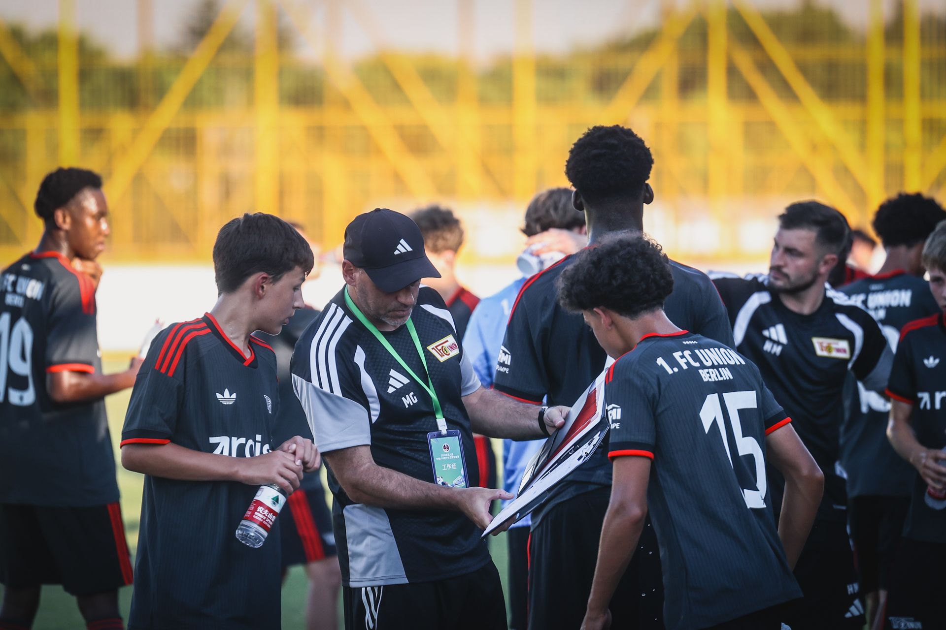 Ein Trainer bespricht sich mit jungen Spielern eines Fußballteams, während andere Teammitglieder in der Nähe warten.