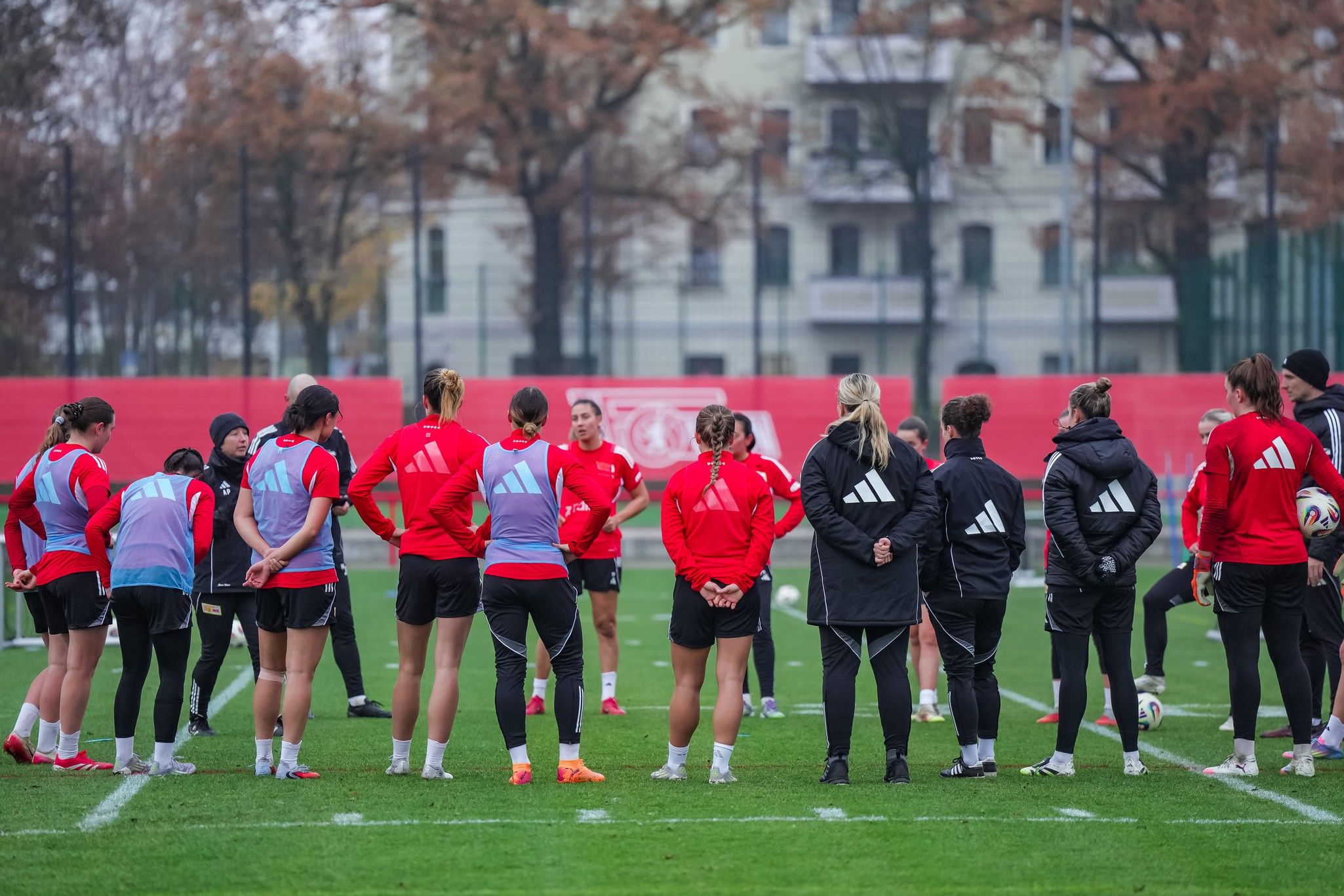 Gruppierung von Fußballspielerinnen in roten Trikots während eines Trainings auf einem grünen Feld.