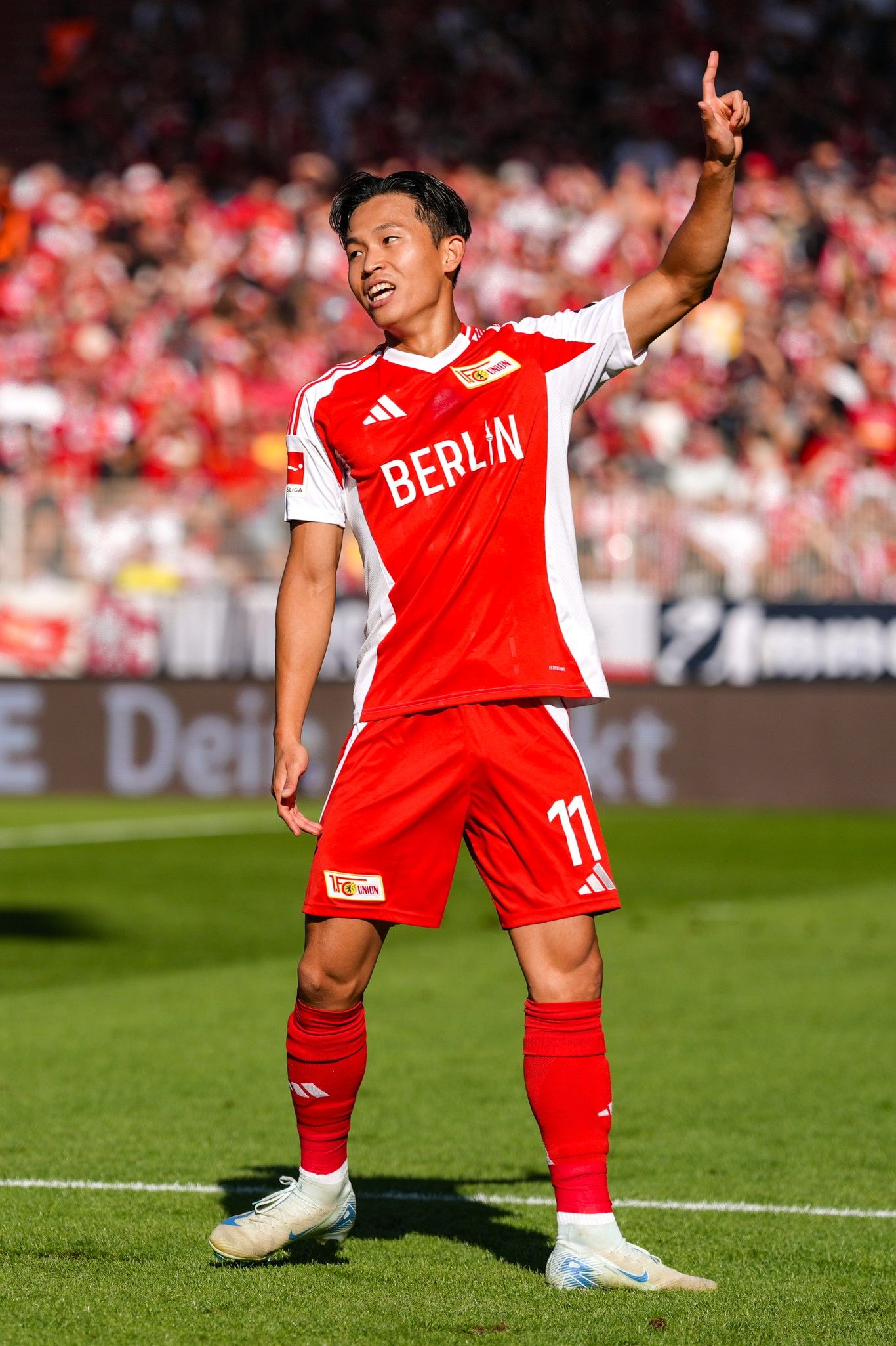 Fußballspieler in rotem Trikot mit der Nummer 11, feiert einen Treffer vor jubelndem Publikum im Stadion.