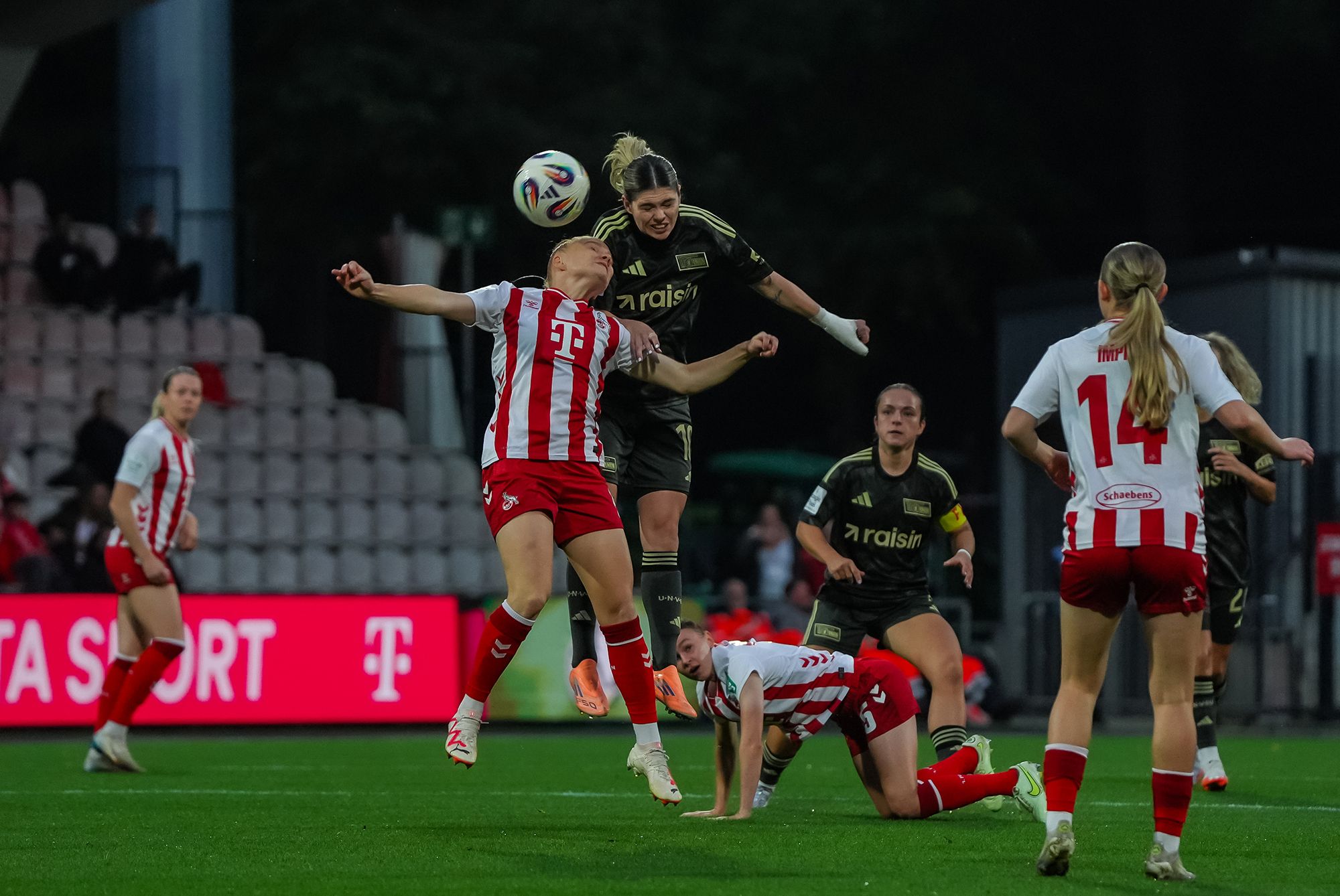 Eine Spielerin springt hoch, um den Ball zu köpfen, während zwei andere Spielerinnen auf dem Feld in Aktion sind.