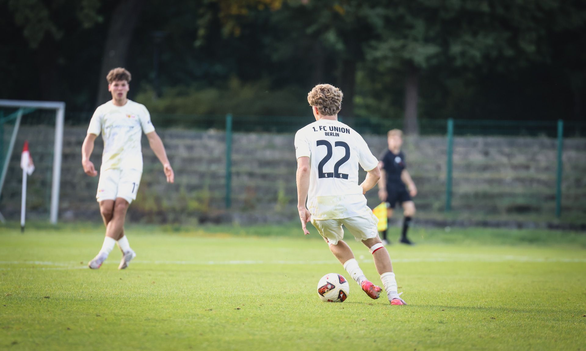 Zwei Fußballspieler auf einem Spielfeld, einer dribbelt den Ball, während der andere in der Nähe steht.