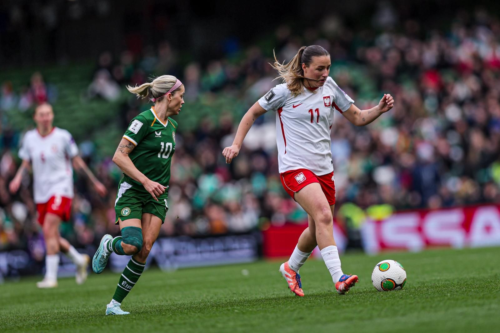 Zwei Frauenfußballspielerinnen in Aktion auf dem Spielfeld während eines Spiels, im Hintergrund eine Zuschauertribüne.