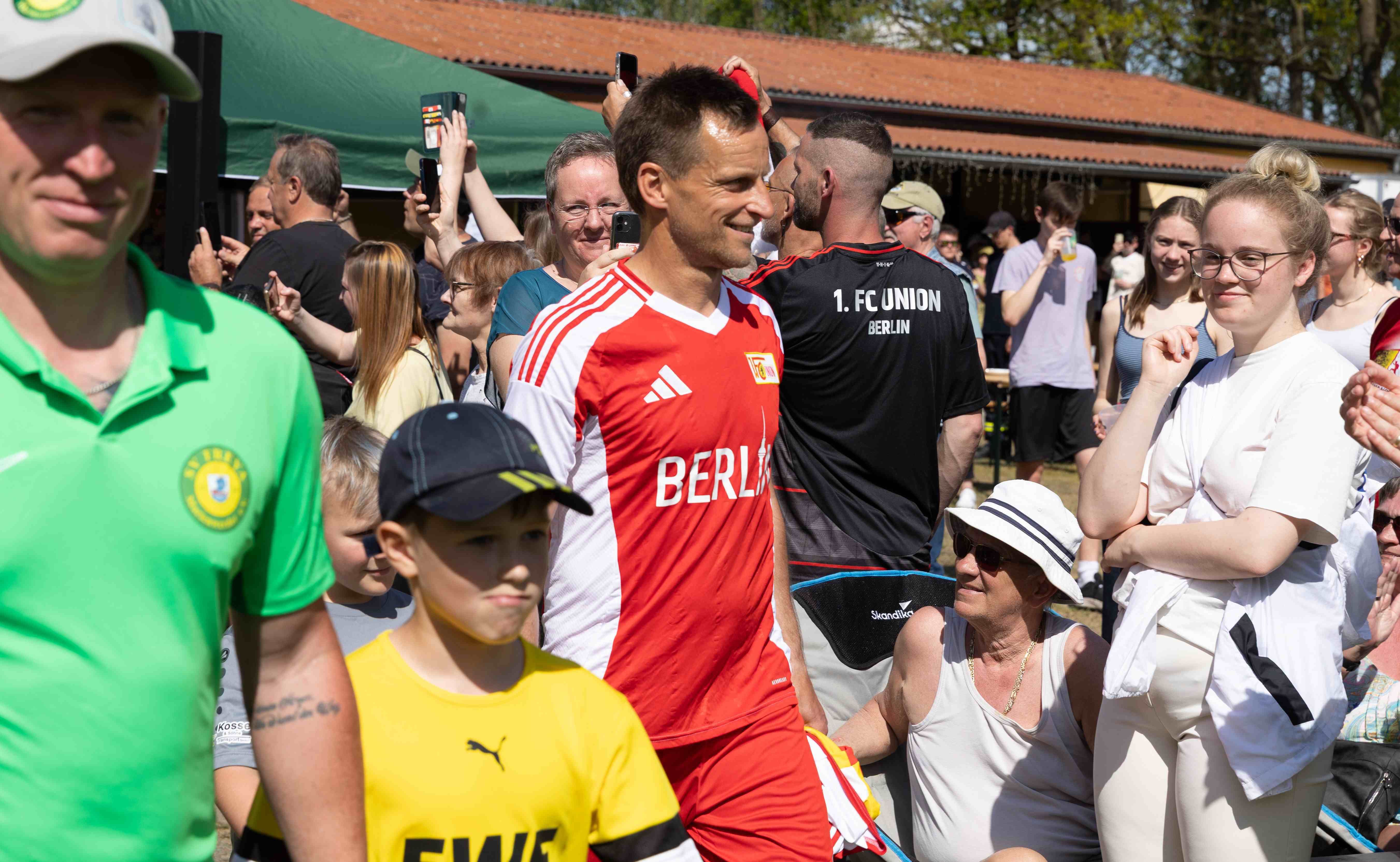 Ein Fußballtorwart in rot-weißem Trikot geht durch eine Menschenmenge, während Zuschauer ihn anfeuern.