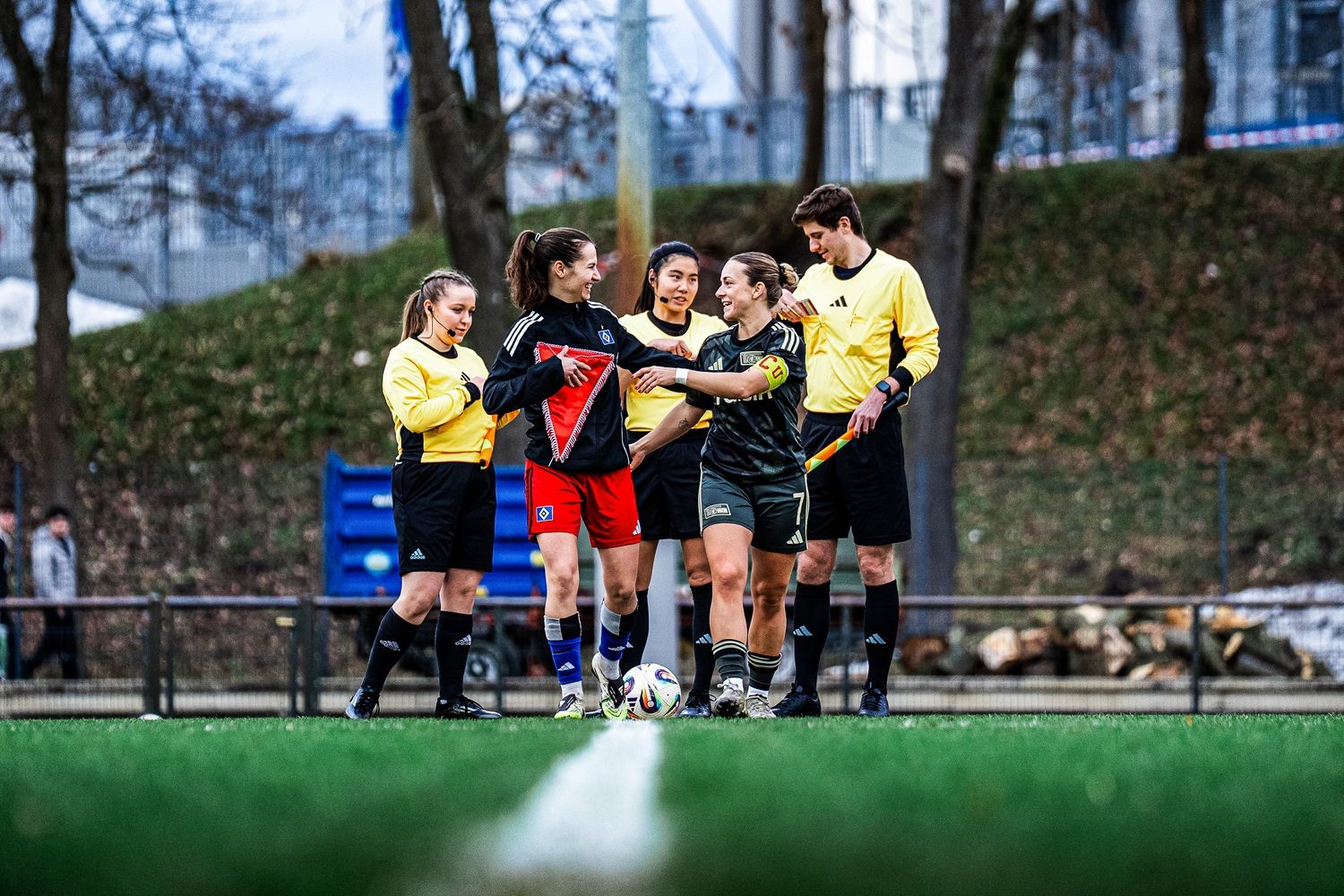 Zwei Fußballmannschaften und Schiedsrichter auf dem Spielfeld, während sie strategisch die Aufstellung besprechen.