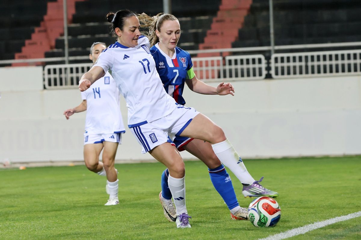 Zwei Fußballspielerinnen im Wettkampf um den Ball auf einem Spielfeld. Die Spielerinnen tragen Trikots in Blau und Weiß.