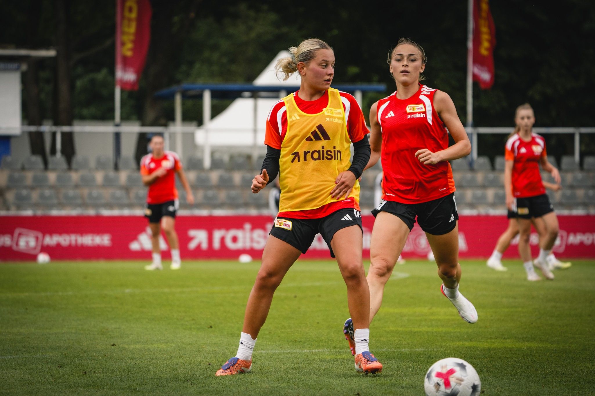 Zwei Fußballspielerinnen trainieren auf einem Platz, eine trägt ein gelbes Trikot, die andere ein rotes Trikot.