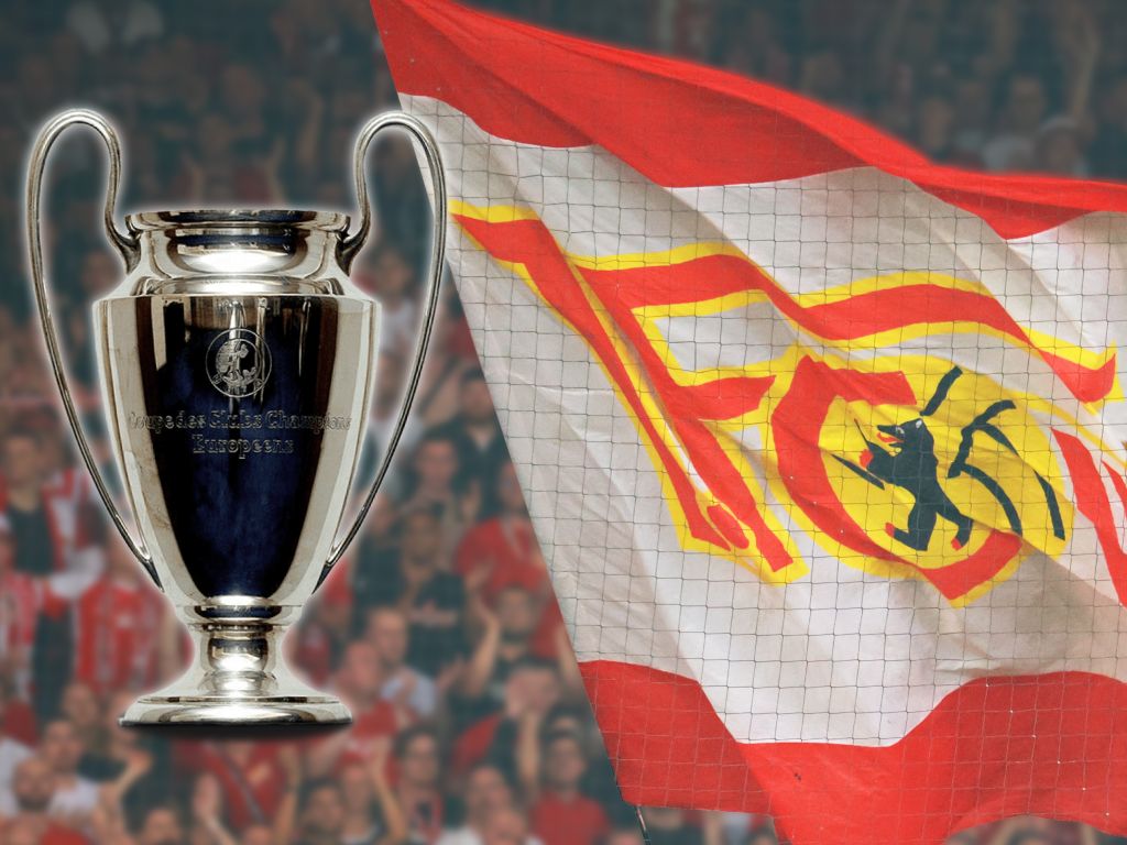 Champions League trophy next to a flag with the Union Berlin logo, with cheering fans in the background.