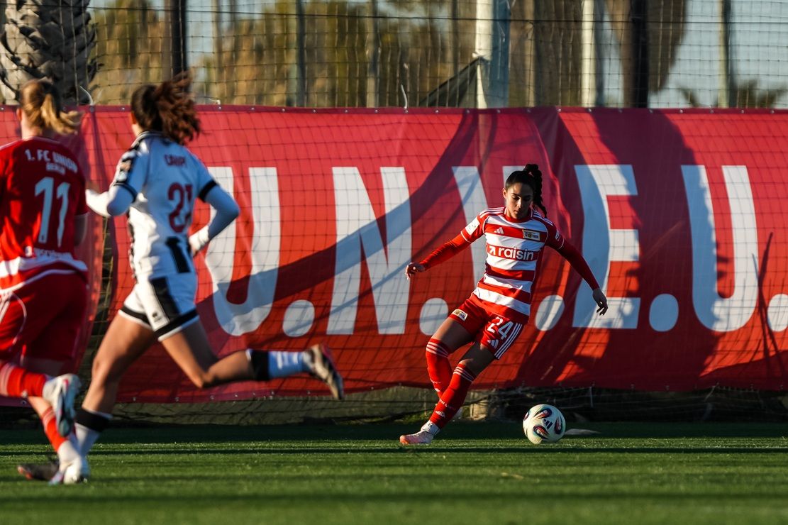 Eine Fußballspielerin in rotem Trikot bereitet sich darauf vor, den Ball zu spielen, während andere Spielerinnen im Hintergrund zu sehen sind.
