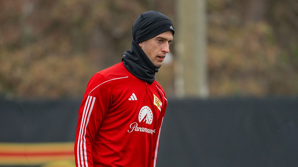 Ein Fußballspieler in einem roten Trainingsanzug und schwarzem Beanie während des Trainings auf dem Platz.