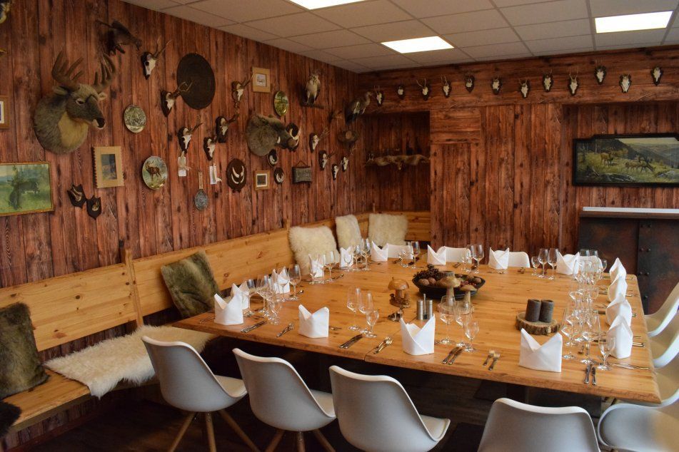 Ein rustikaler Essraum mit Holzwänden, einem großen Tisch und Jagdtrophäen an den Wänden, festlich eingedeckt für ein Essen.